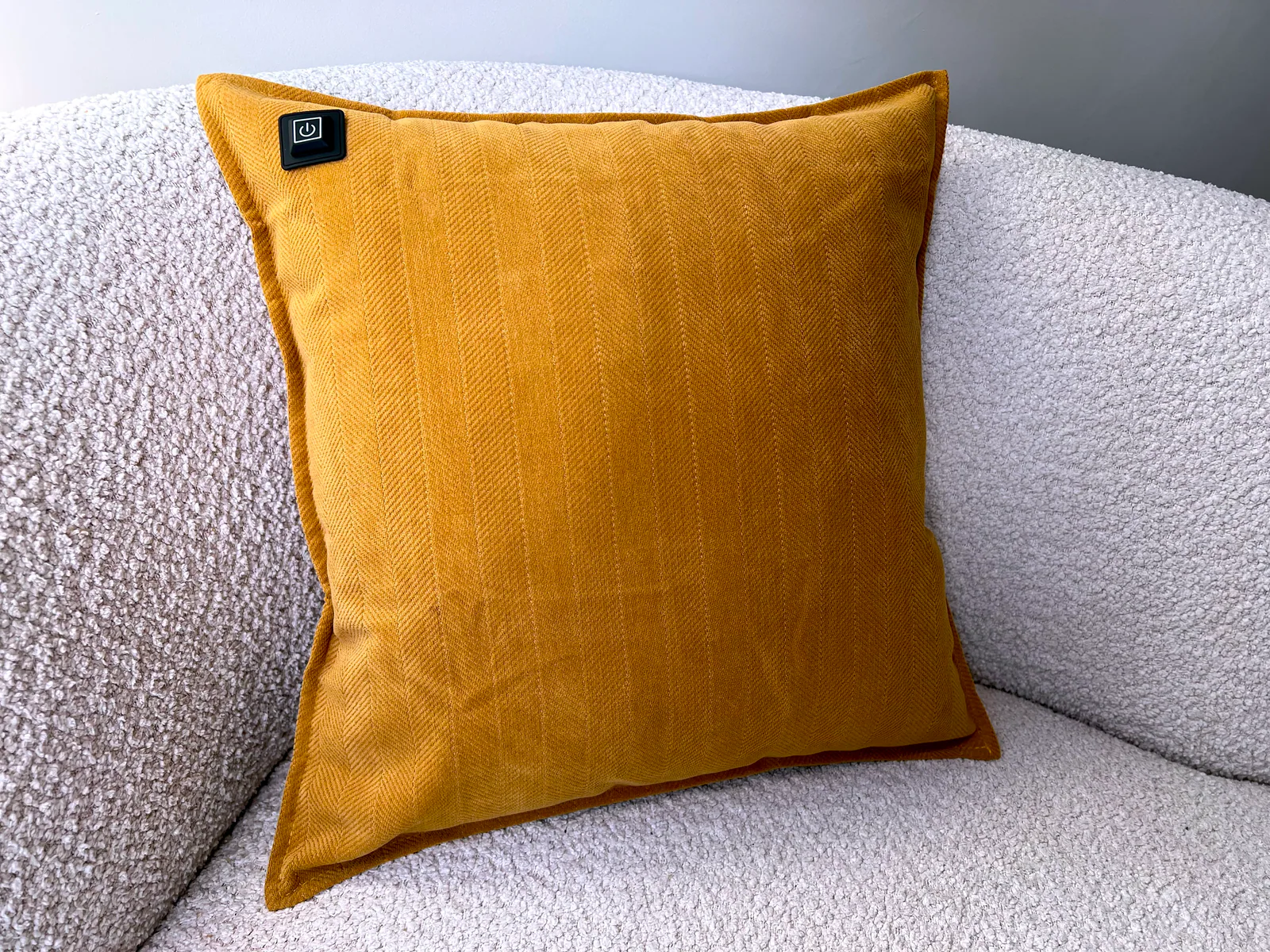 Ein ockergelbes Kissen mit Fischgrätmuster liegt auf einem weißen Bouclé-Sofa.