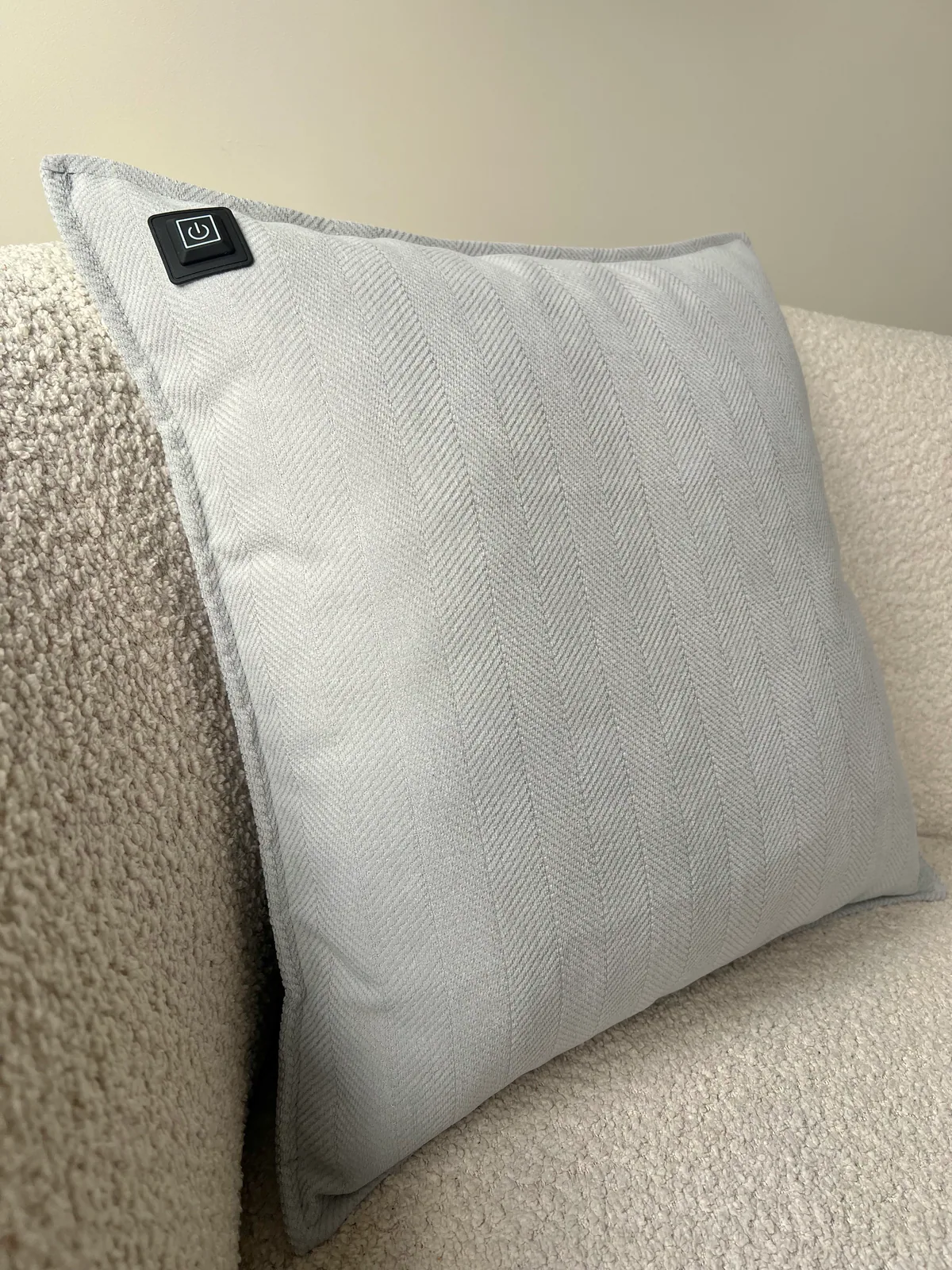 Graues Kissen mit Fischgrätmuster und Power-Symbol auf einem Sofa.