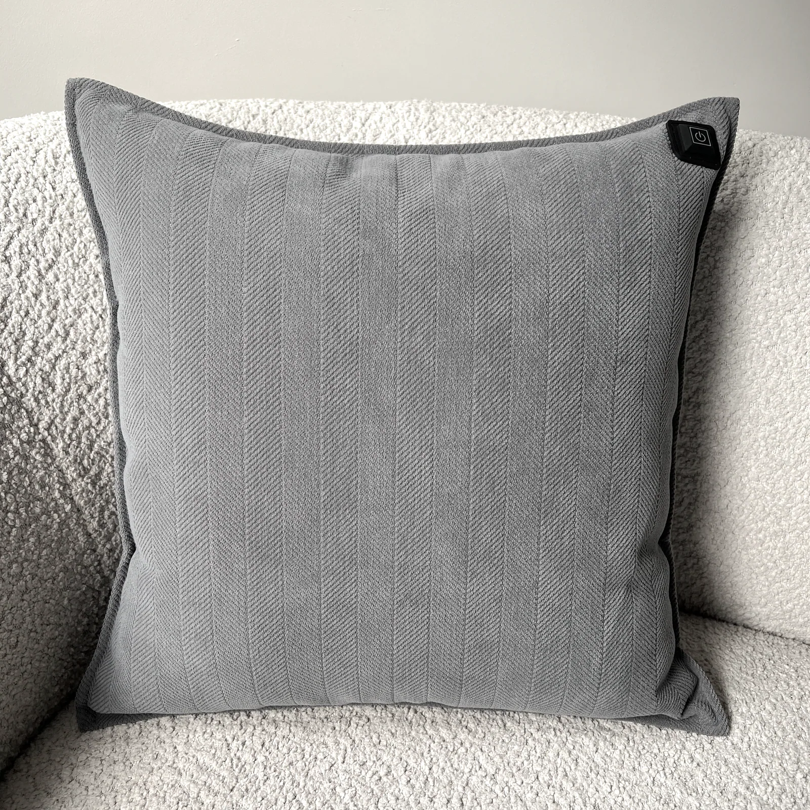 Graues Kissen mit Fischgrätmuster auf einem cremefarbenen Sofa. Oben rechts ist ein schwarzer Knopf.