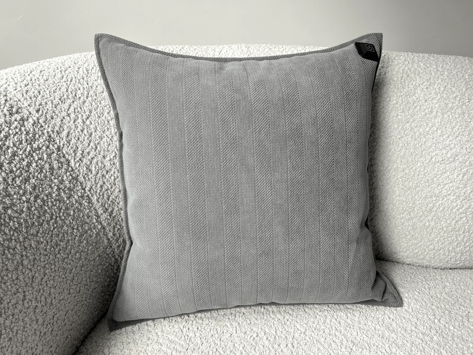 Graues Kissen mit Fischgrätmuster auf einem weißen Bouclé-Sofa.