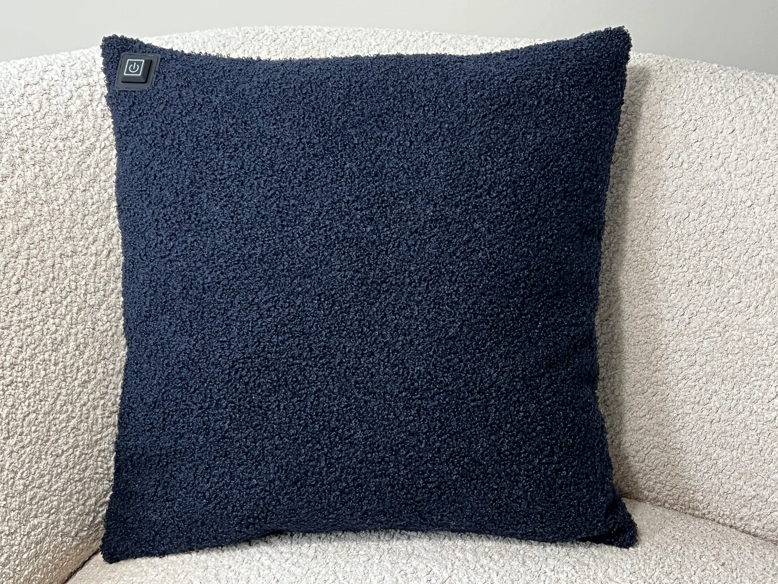 Ein dunkelblaues Kissen mit Teddy-Stoff liegt auf einem hellen Sofa. Ein Energiesymbol ist sichtbar.