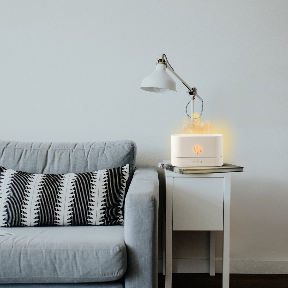 Ein weißer Diffusor mit Flammen-Effekt steht auf einem Nachttisch neben einem Sofa.