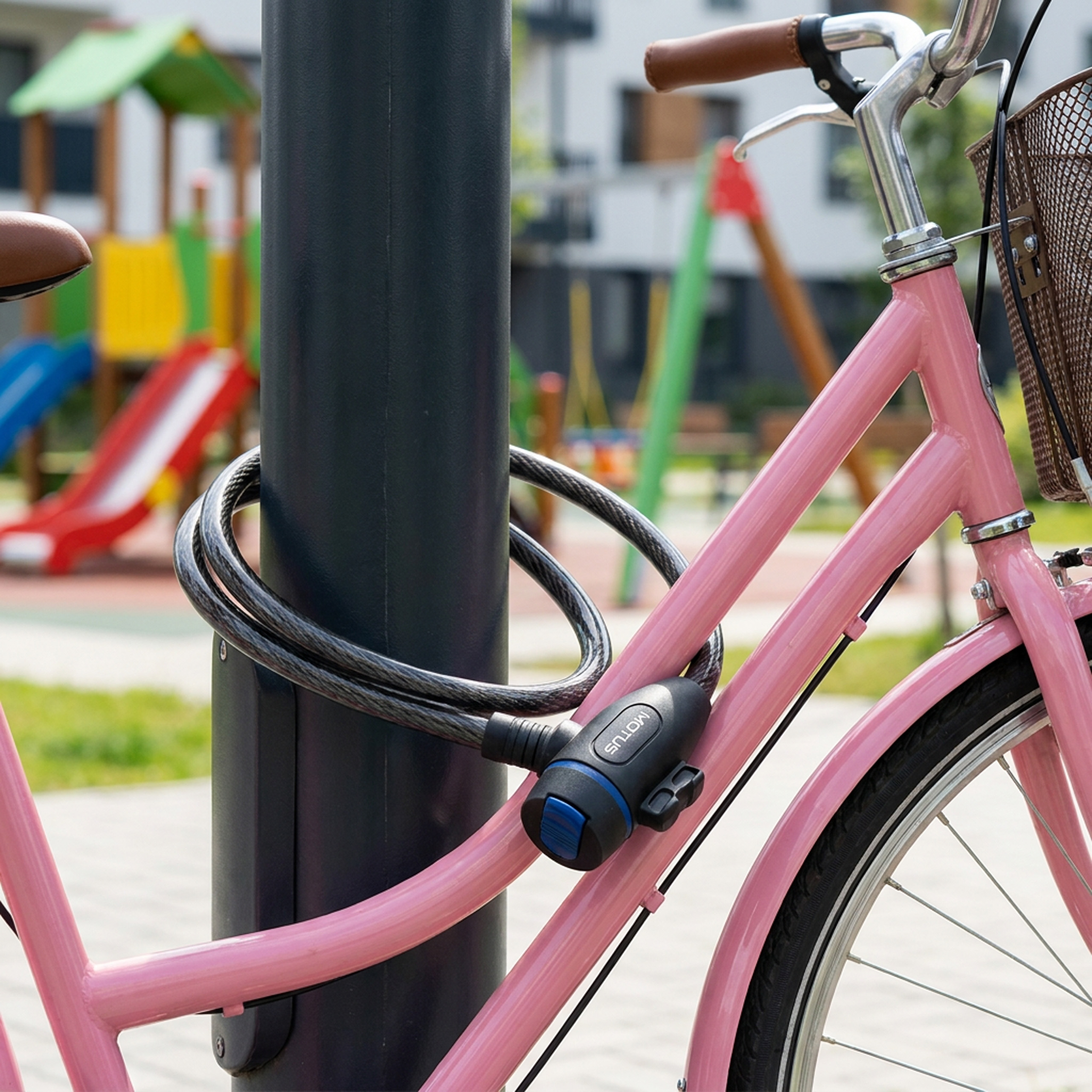 Una bicicletta rosa è legata a un lampione con un lucchetto. Parco giochi sullo sfondo.