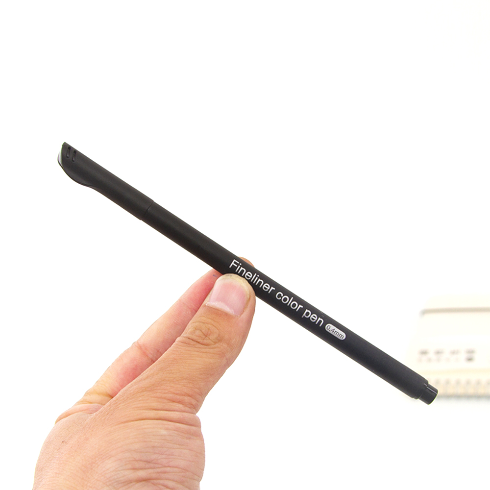Una mano tiene una penna fineliner nera con la scritta "Fineliner color pen 0.4mm".