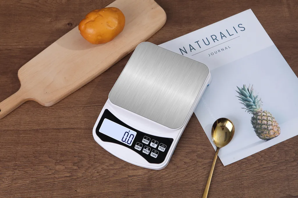 Eine digitale Küchenwaage mit einem Brot, einer Ananas und einem Löffel auf einem Holztisch.