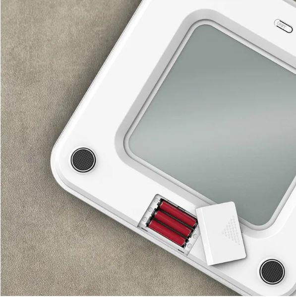 Bilancia bianca con vano batteria aperto e tre batterie rosse.