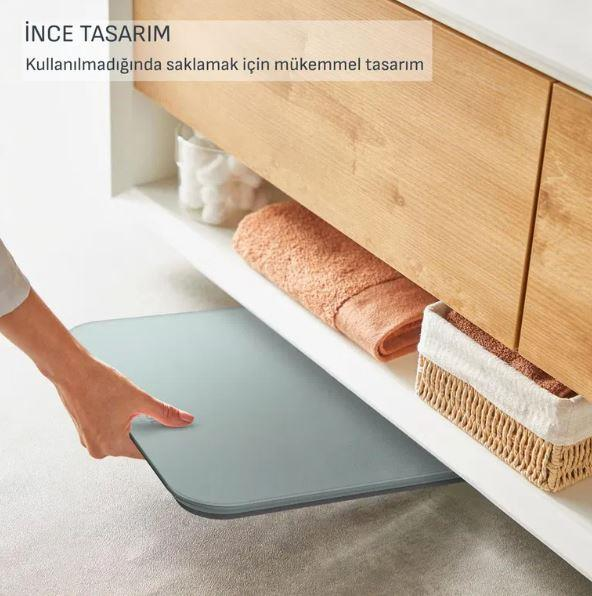Una mano estrae un sottile tappeto grigio da sotto una mensola con asciugamani.