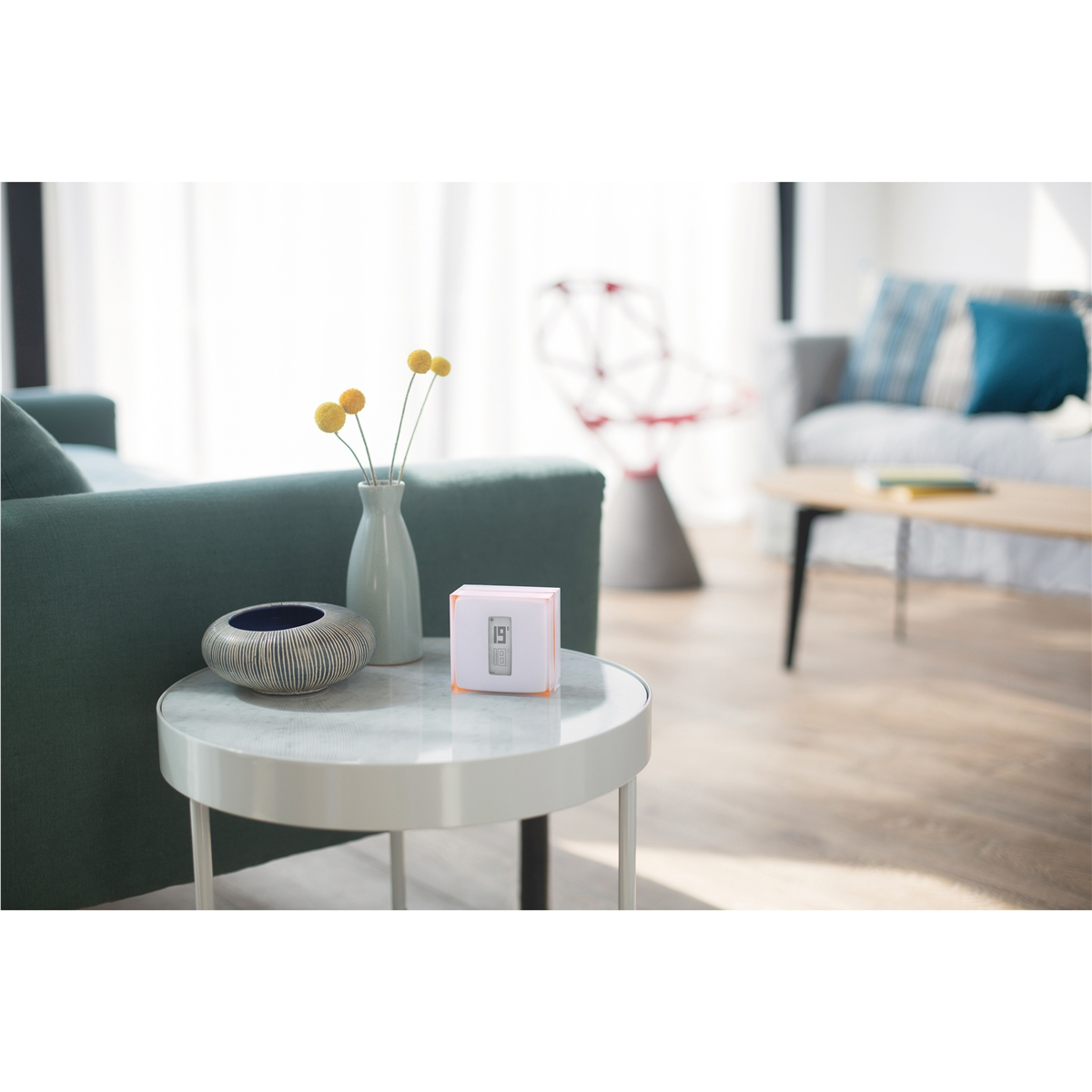 Un cubo blanco con pantalla se sienta en una mesa auxiliar junto a un jarrón de flores amarillas.