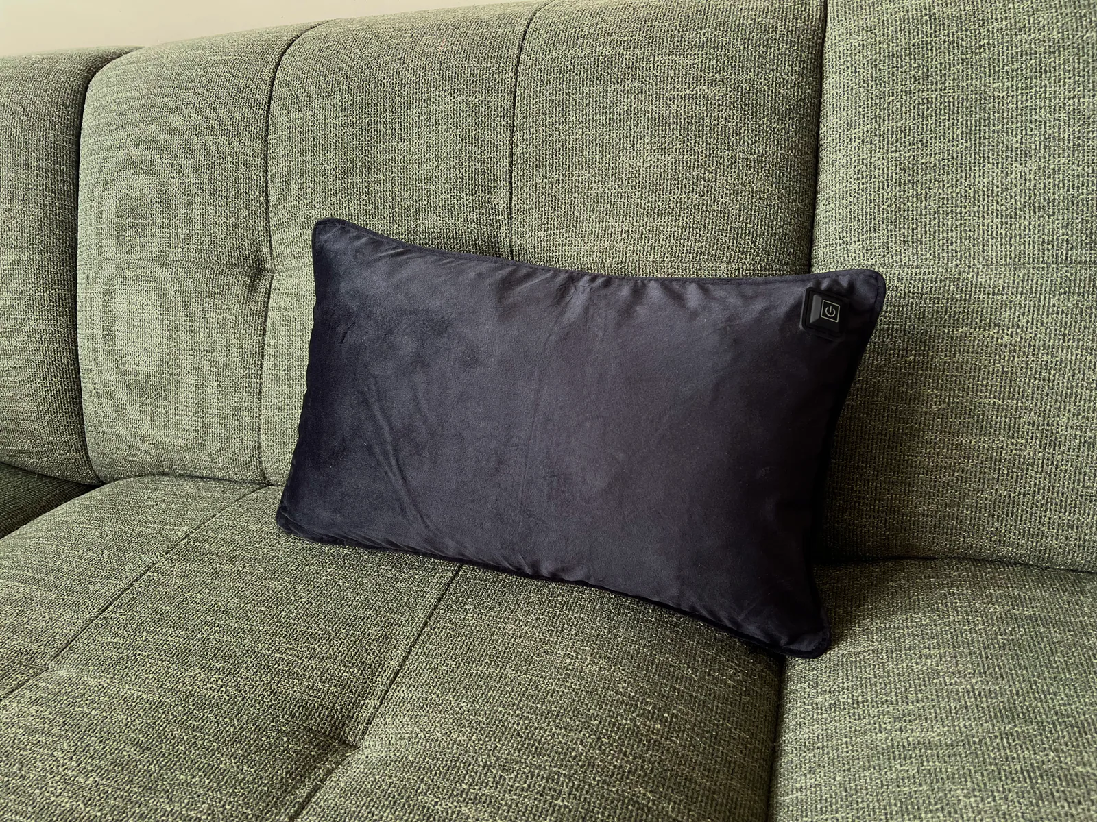 Ein dunkles Kissen mit einem Power-Symbol liegt auf einem grünen Sofa.