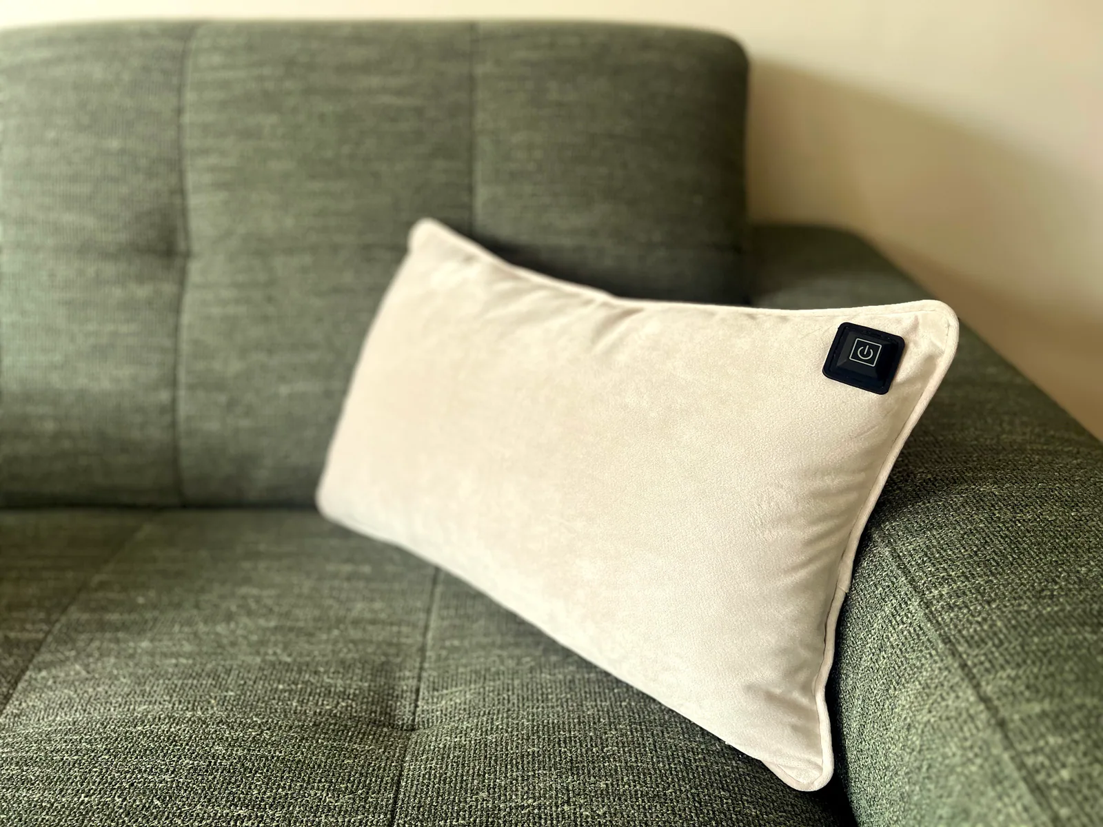 Ein helles Kissen mit einem schwarzen Power-Symbol liegt auf einem grünen Sofa.