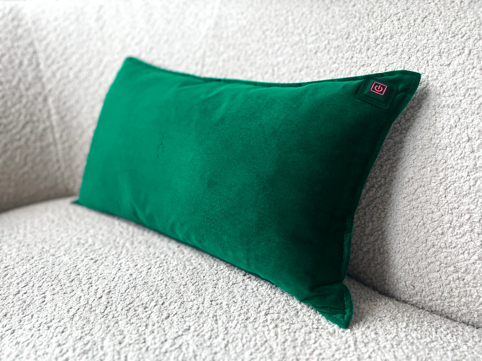 Ein grünes Samtkissen mit Power-Symbol ruht auf einer texturierten weißen Couch.