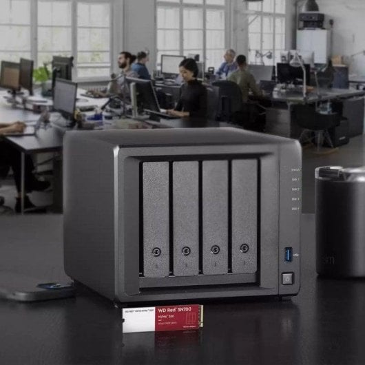 Un dispositivo NAS nero a quattro vani è su una scrivania, un SSD davanti. Un ufficio è sfocato sullo sfondo.
