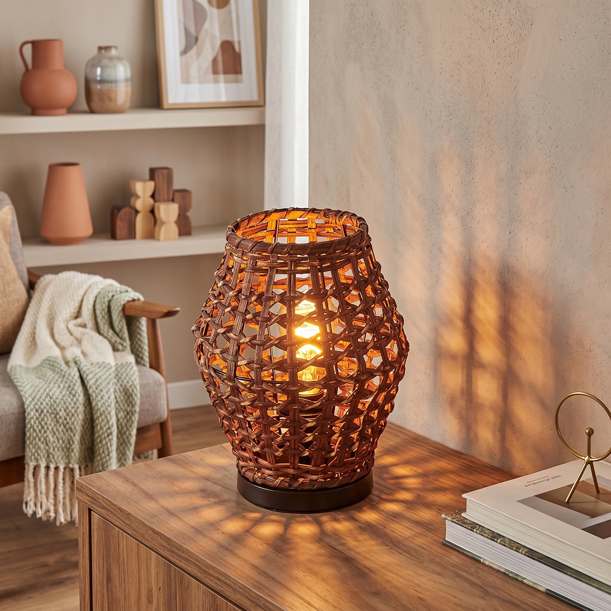 Braune Weidenlampe auf einem Holztisch wirft Schatten. Links ein Sessel mit Decke.