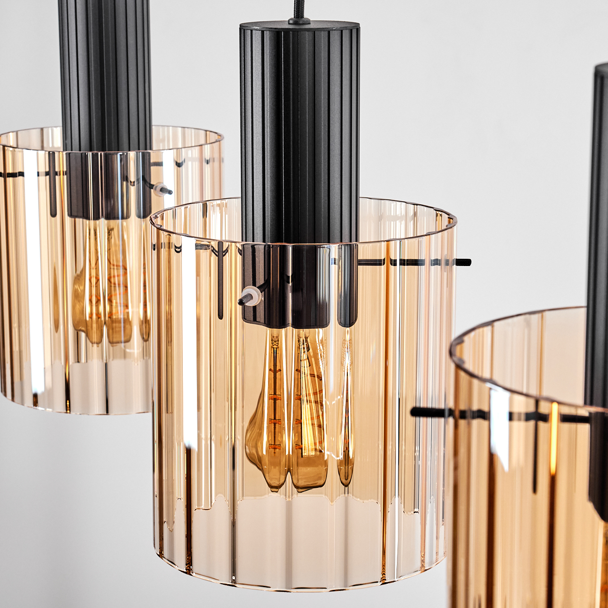 Drei moderne Pendelleuchten mit gerippten schwarzen Metalloberteilen und bernsteinfarbenen Glasschirmen.