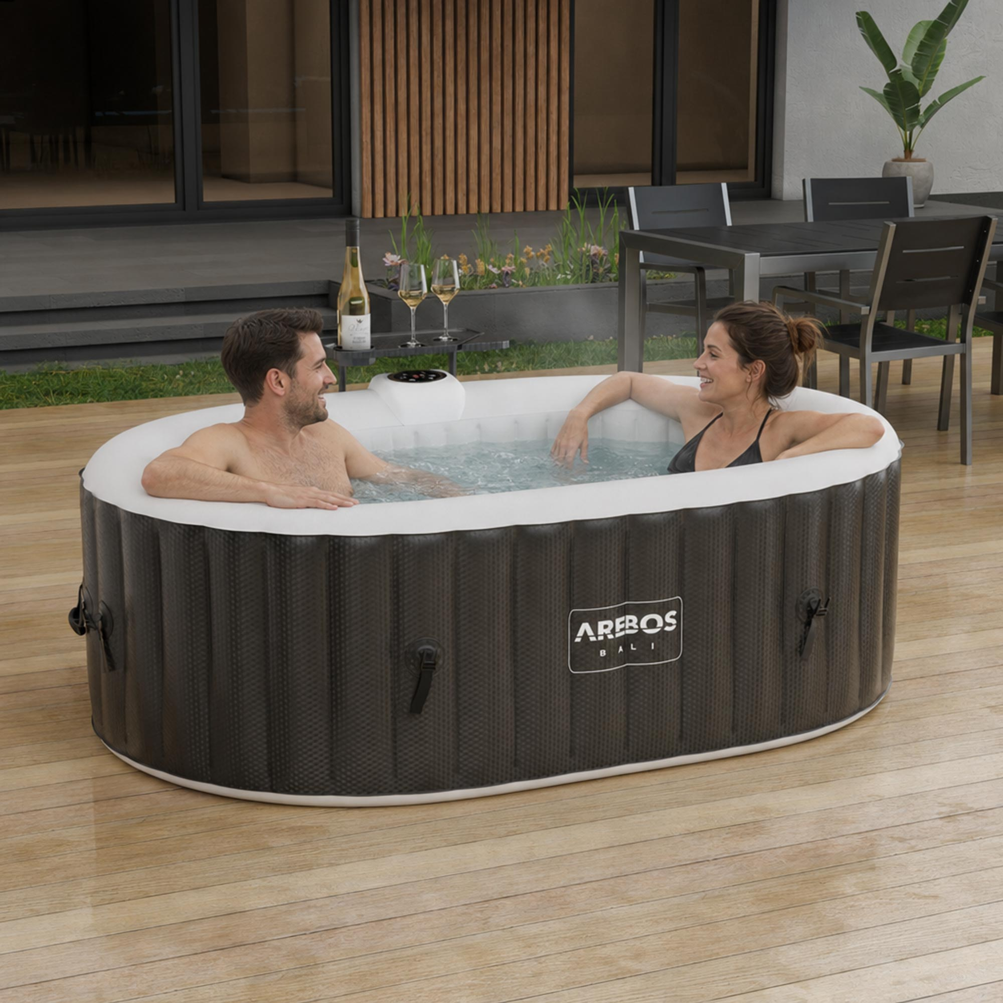 Paar entspannt im Whirlpool auf Holzdeck, im Hintergrund Tisch, Stühle und Pflanzen.