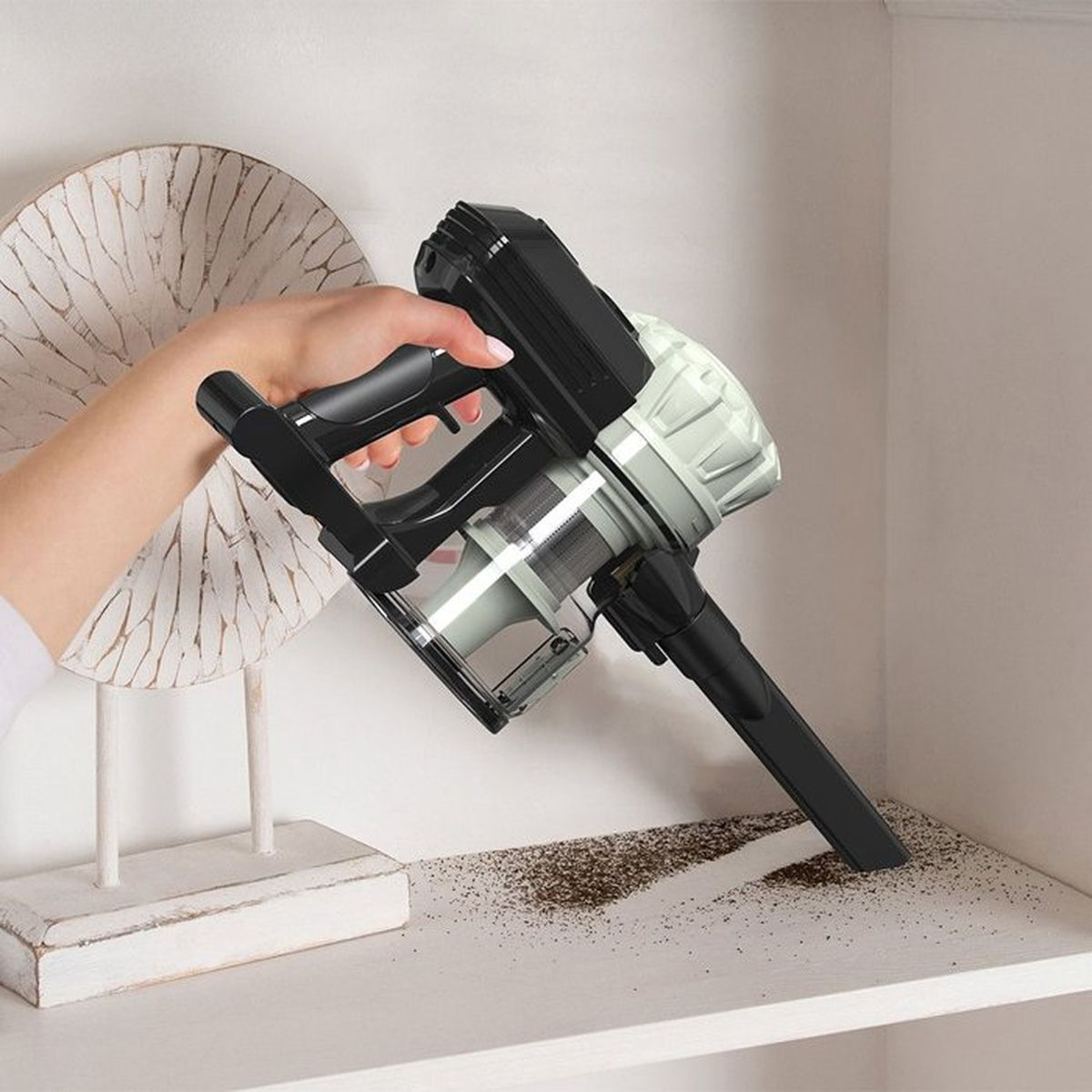 Eine Hand hält einen schwarzen Handstaubsauger, der Staub aufsaugt.