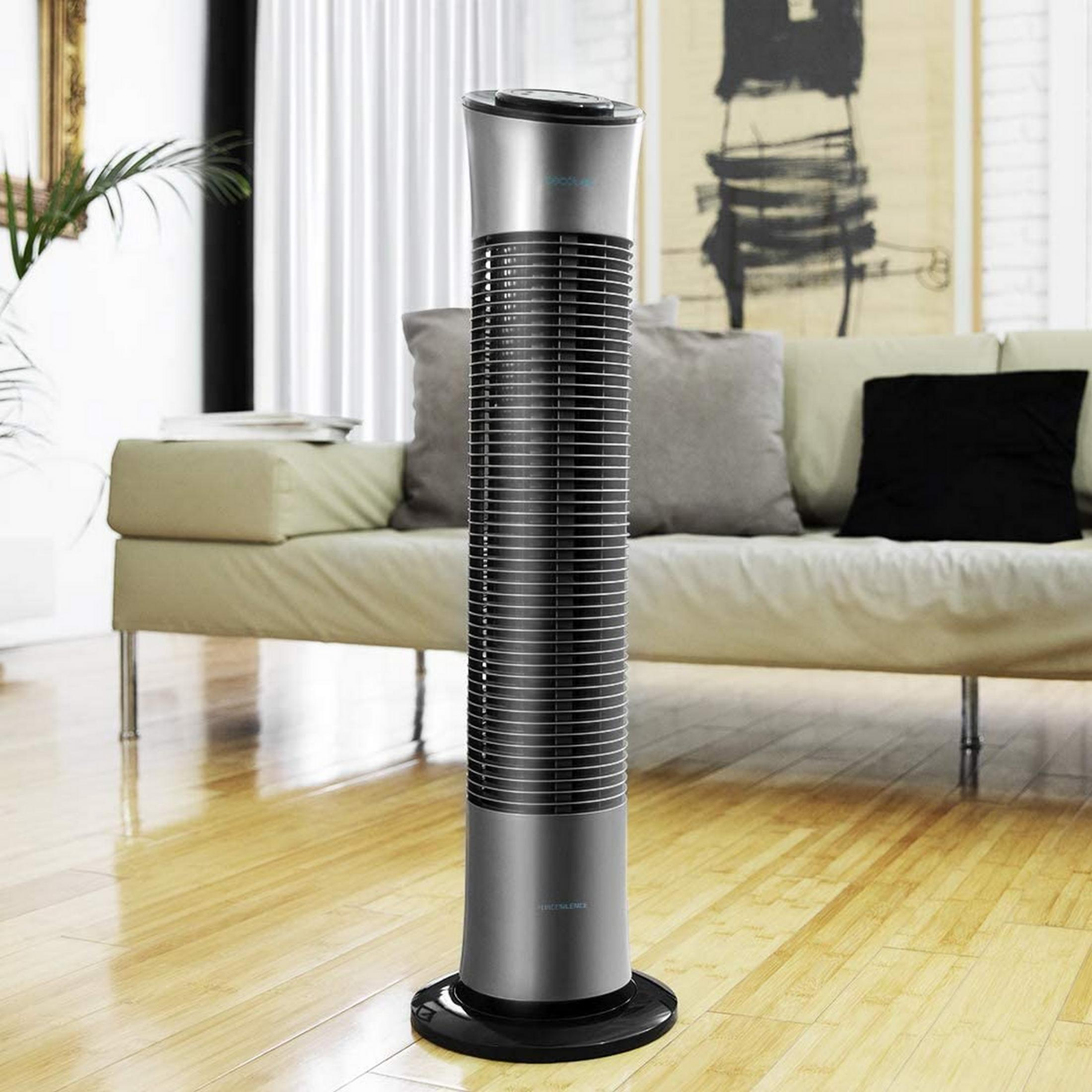 Un elegante ventilador de torre plateado está sobre un suelo de madera frente a un sofá.