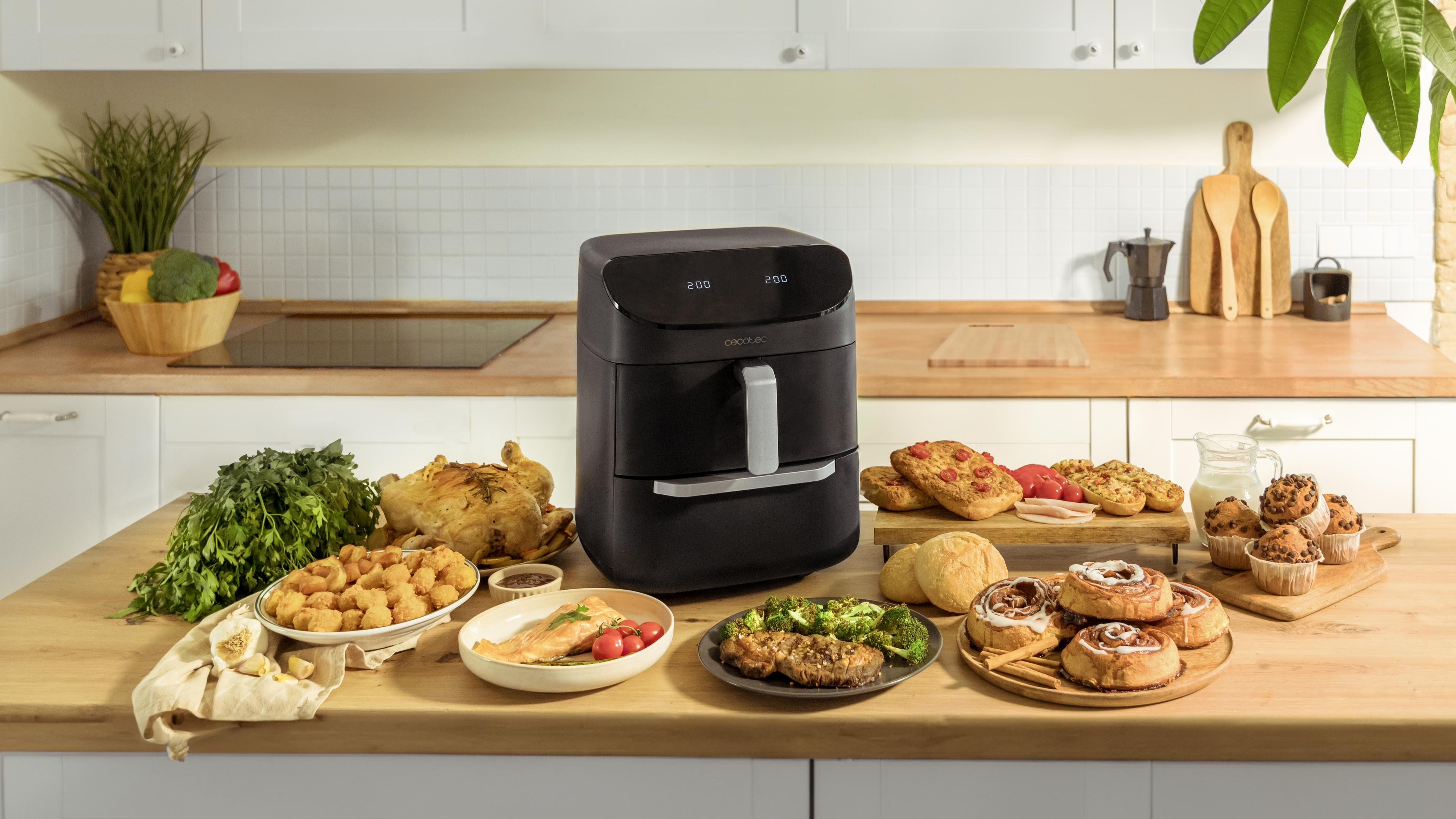 Una friggitrice ad aria nera con vari cibi come pollo arrosto, pesce, carne, panini e muffin.