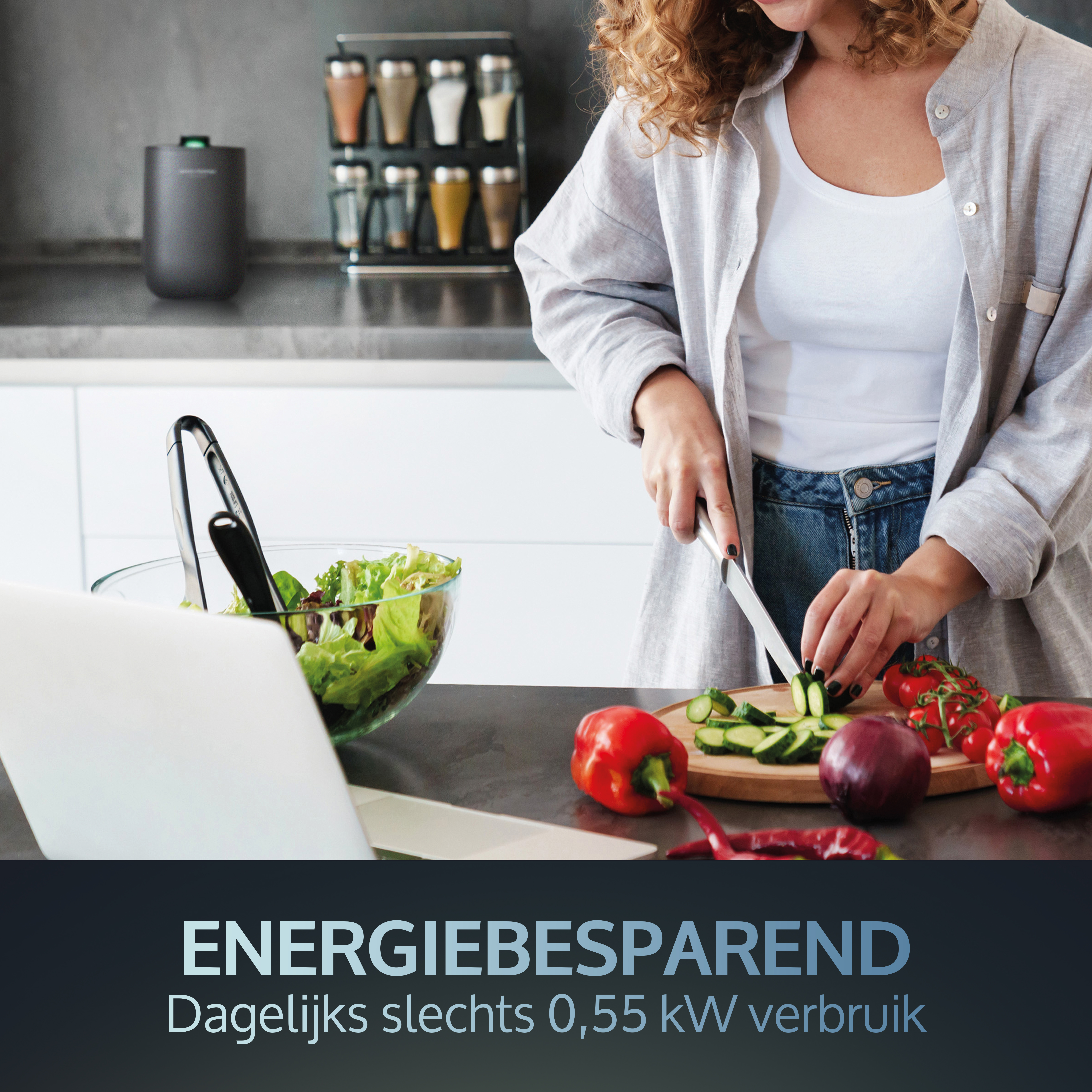 Woman cutting cucumbers in kitchen with laptop, salad, and vegetables on counter.