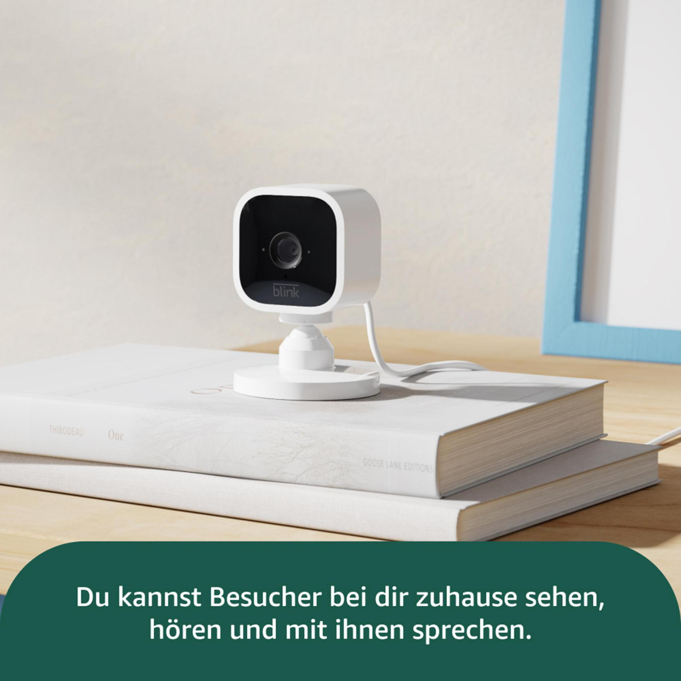 Ein weißer Blink-Kamera-Würfel steht auf Büchern, mit einem blauen Rahmen im Hintergrund.