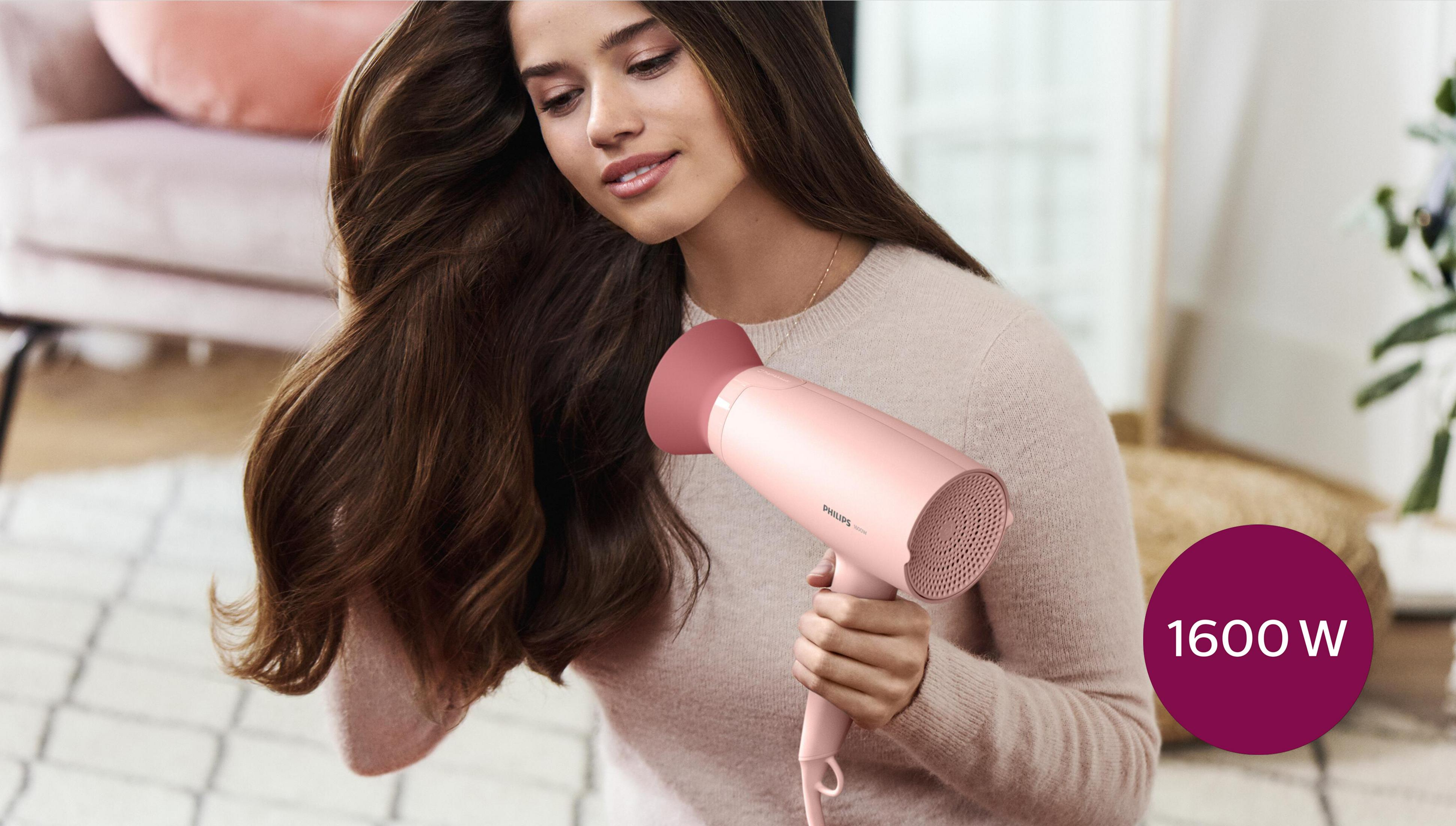 Una donna asciuga i suoi capelli castani con un asciugacapelli rosa Philips.