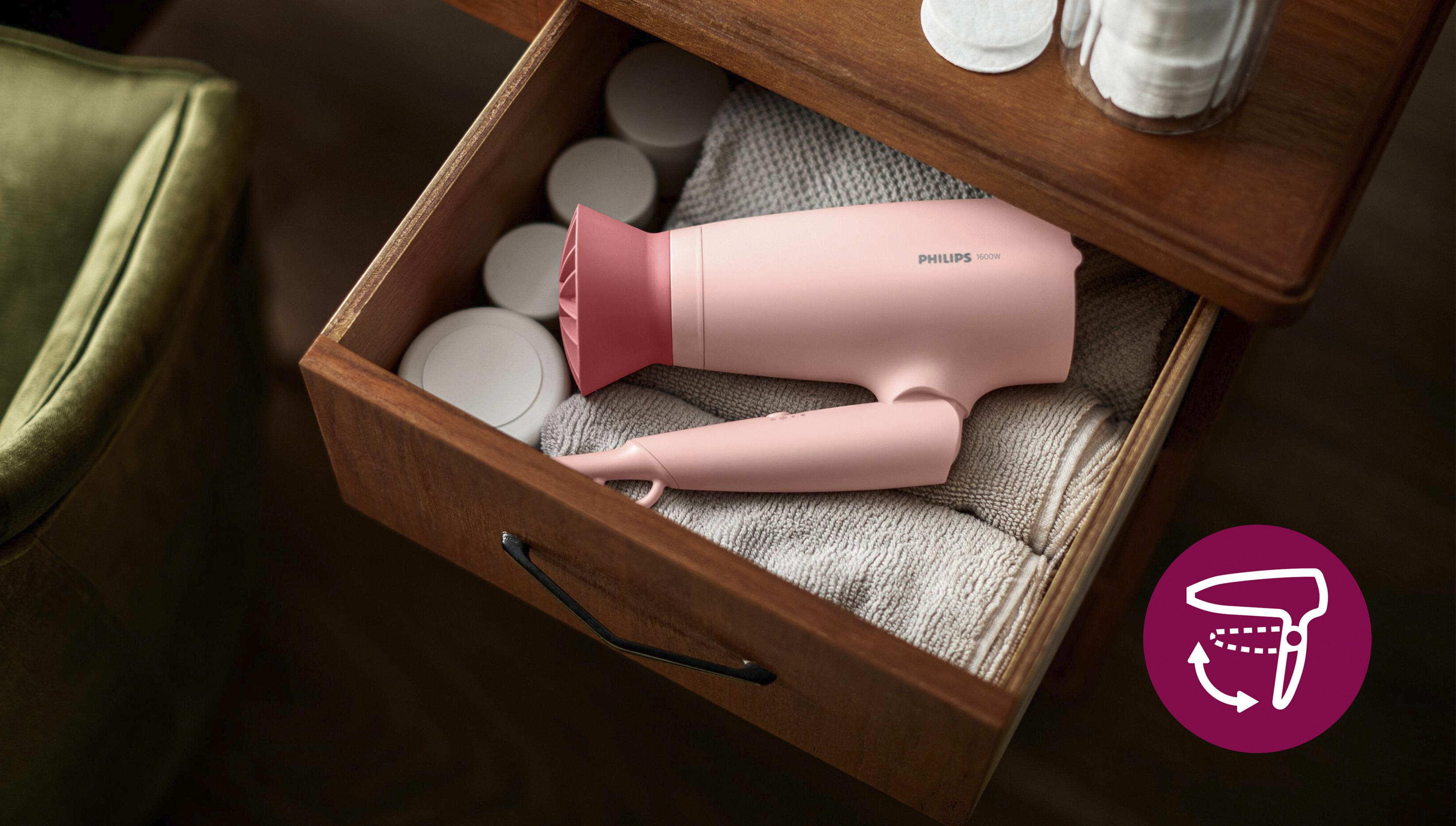 Un asciugacapelli Philips rosa poggia in un cassetto di legno aperto su asciugamani piegati.