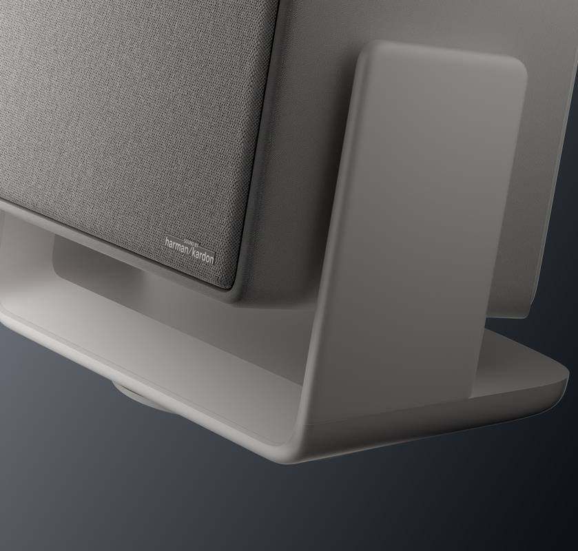 Harman Kardon logolu gri hoparlör beyaz stant üzerinde, koyu arka plan.