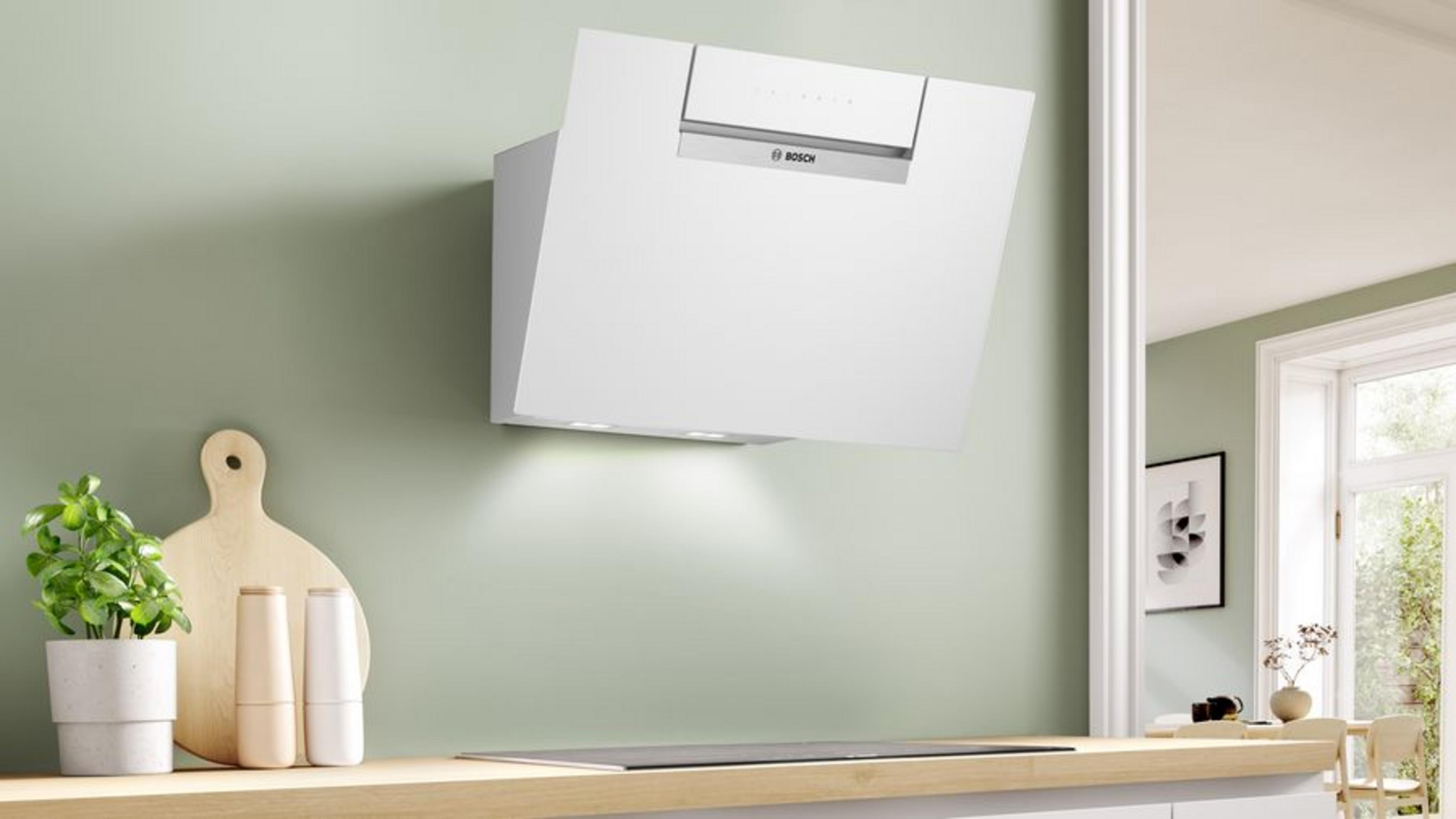Una campana extractora Bosch blanca sobre una placa, con objetos decorativos en un estante.