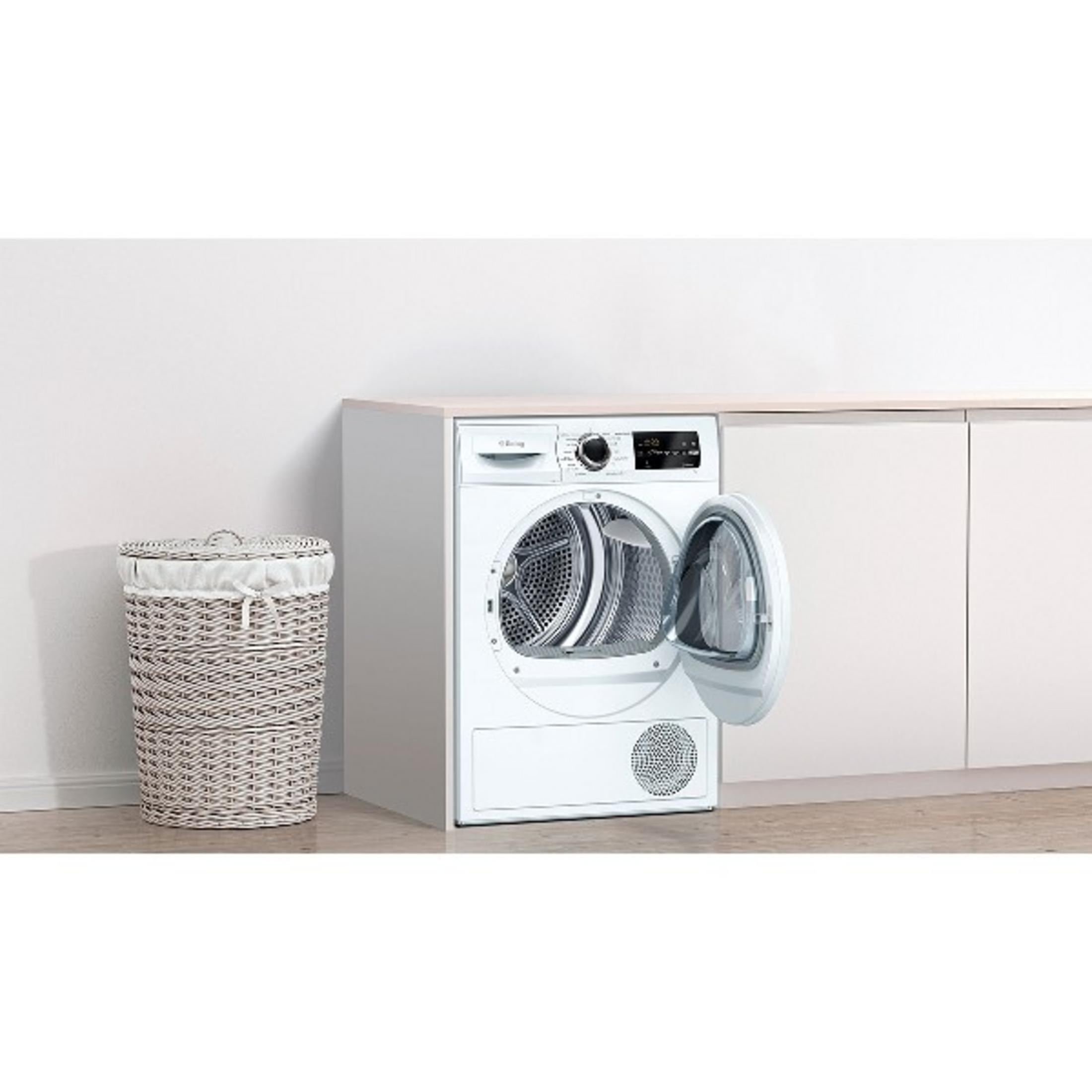 Una cesta de ropa blanca junto a una secadora blanca con la puerta abierta.