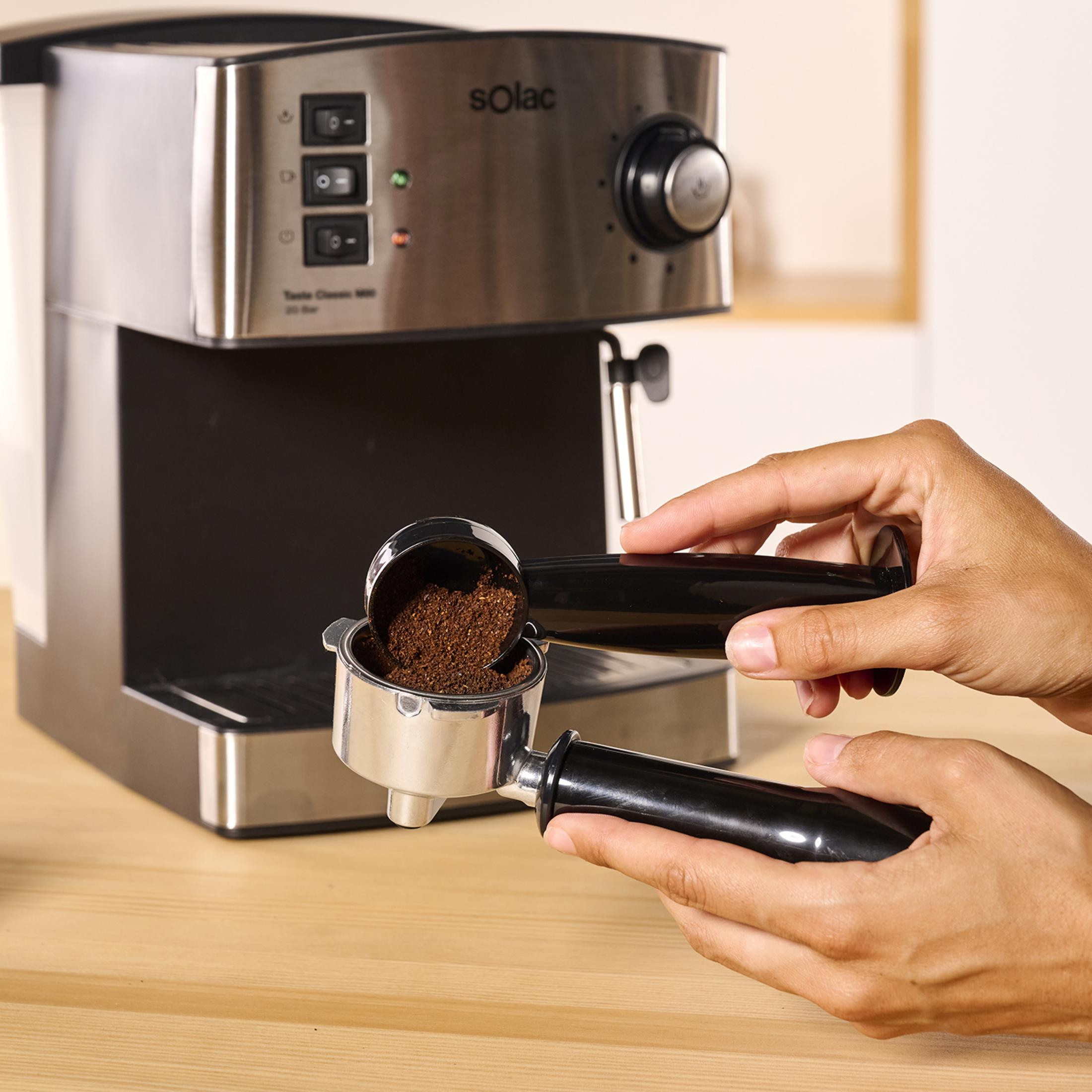 Una mano echa café molido en el portafiltro de una máquina de espresso.
