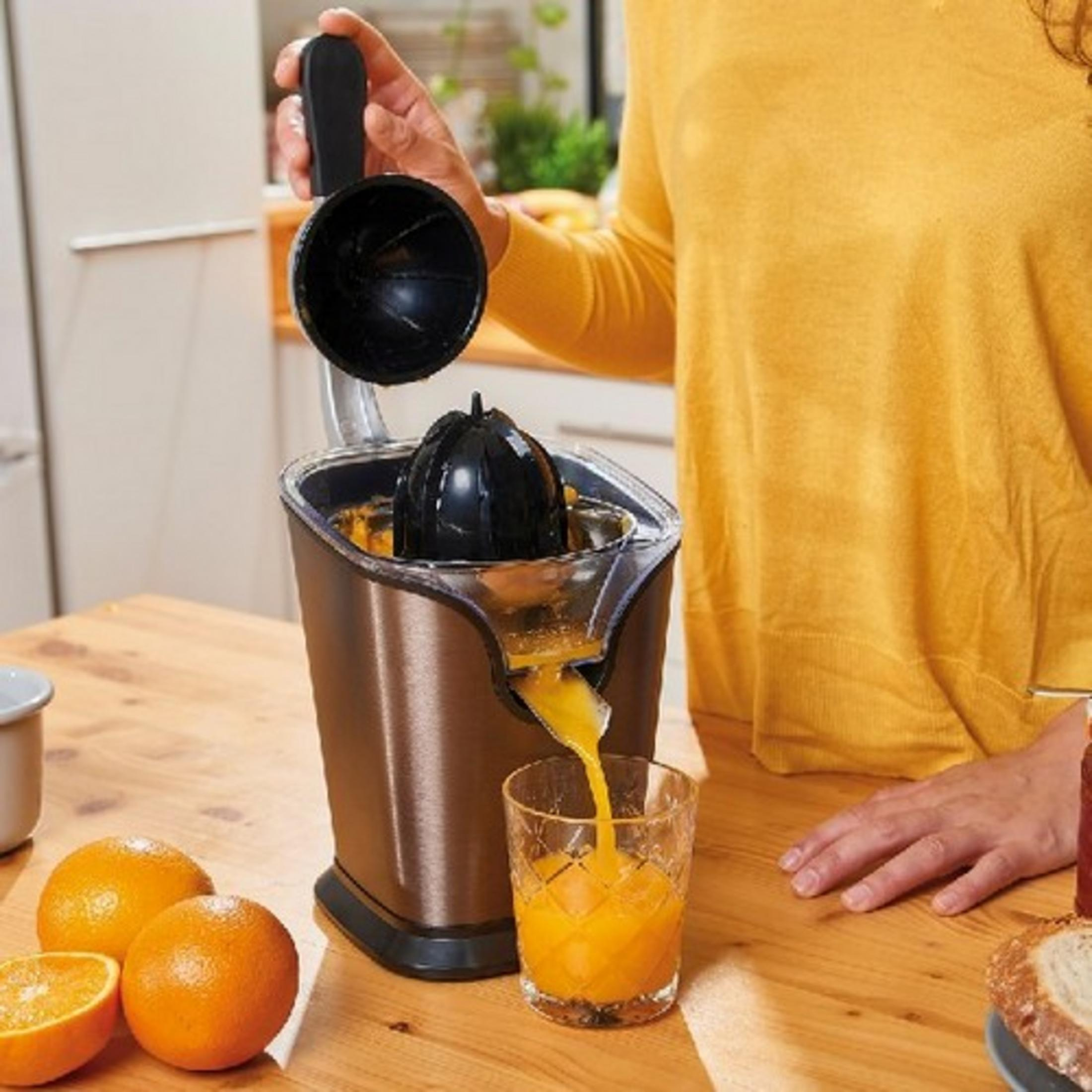 Eine Person presst Orangen mit einem elektrischen Entsafter aus. Frischer Saft fließt in ein Glas.