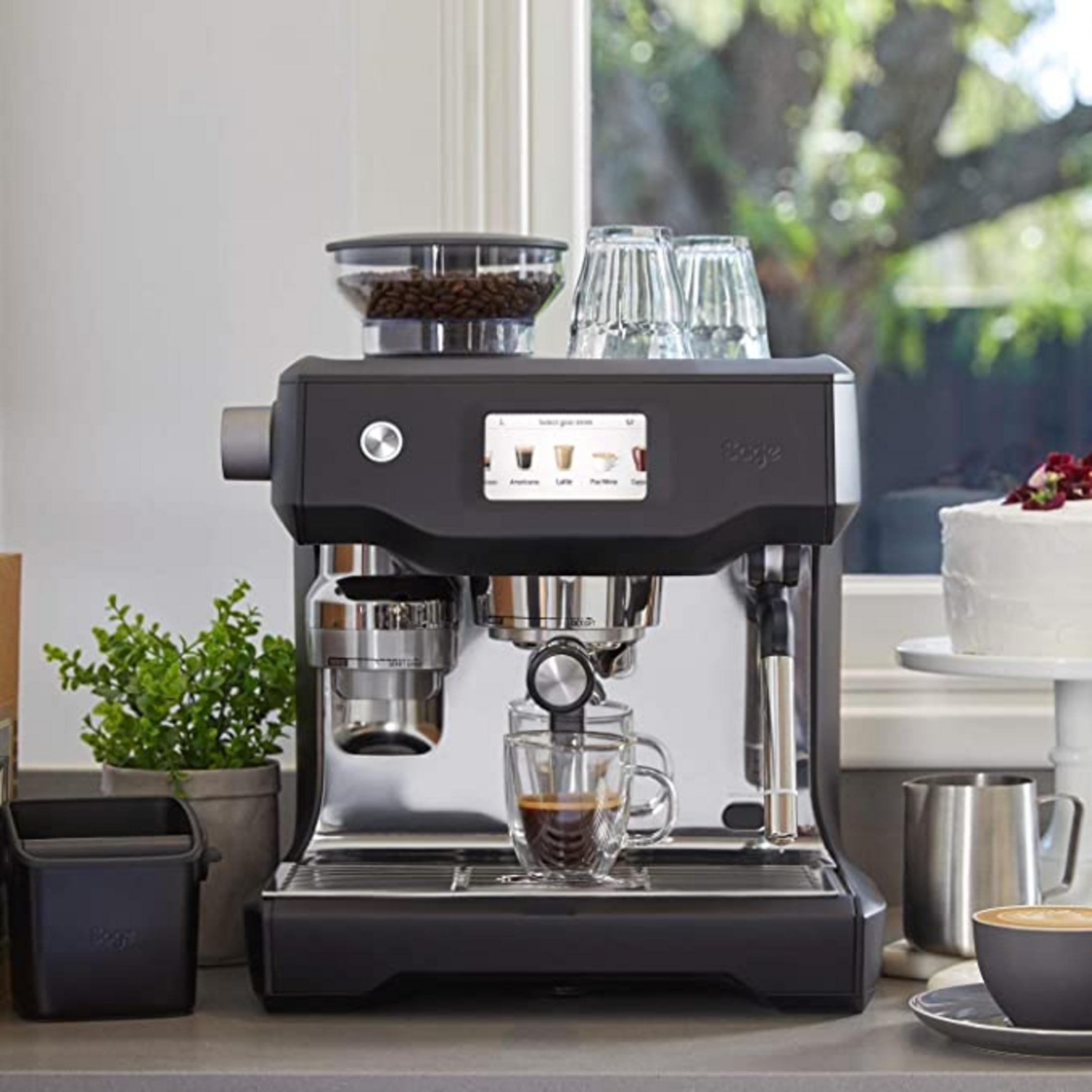 Una macchina per espresso con contenitore per chicchi di caffè, bicchieri, tazza e torta.