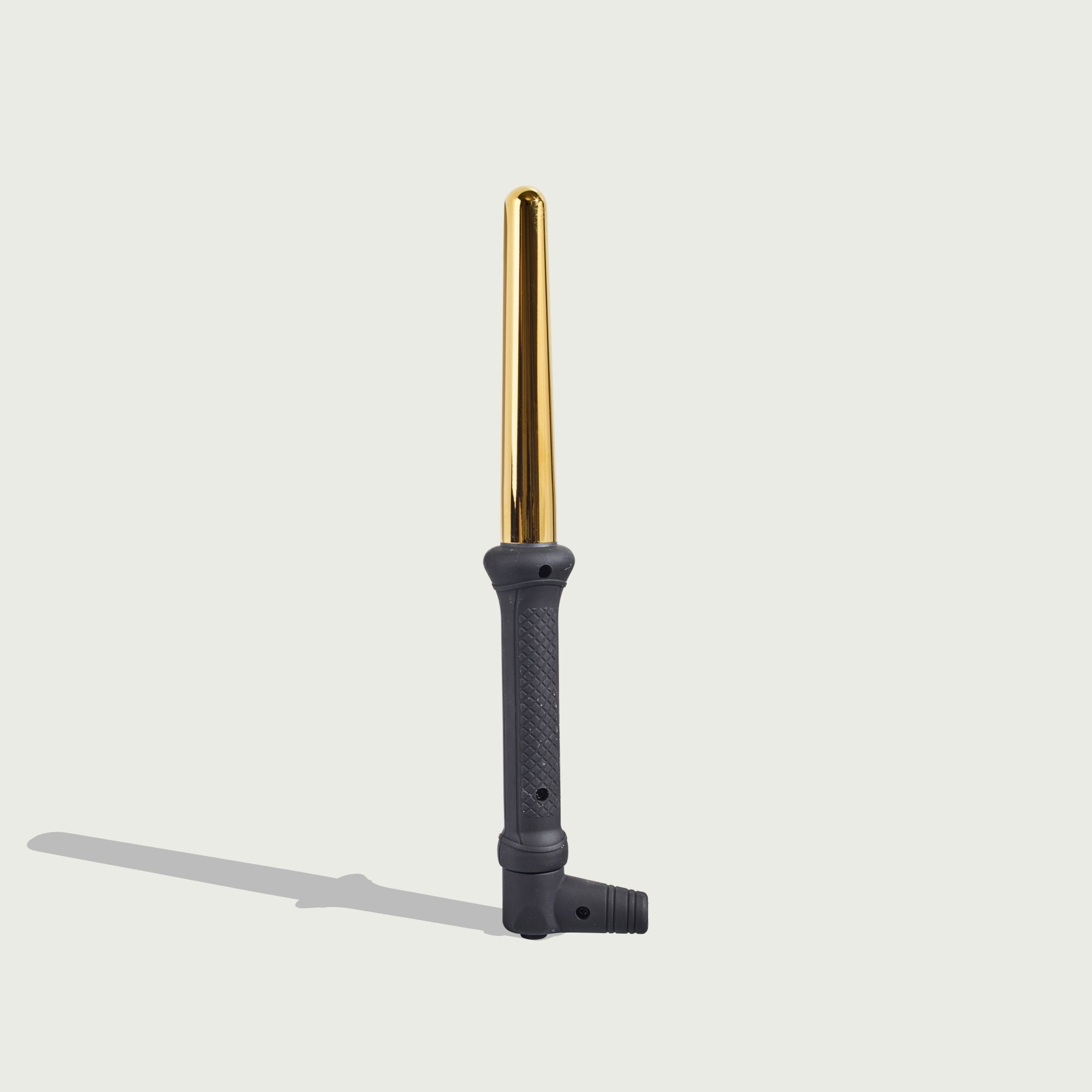 Ein goldener Lockenstab mit schwarzem Griff liegt auf hellem Untergrund.
