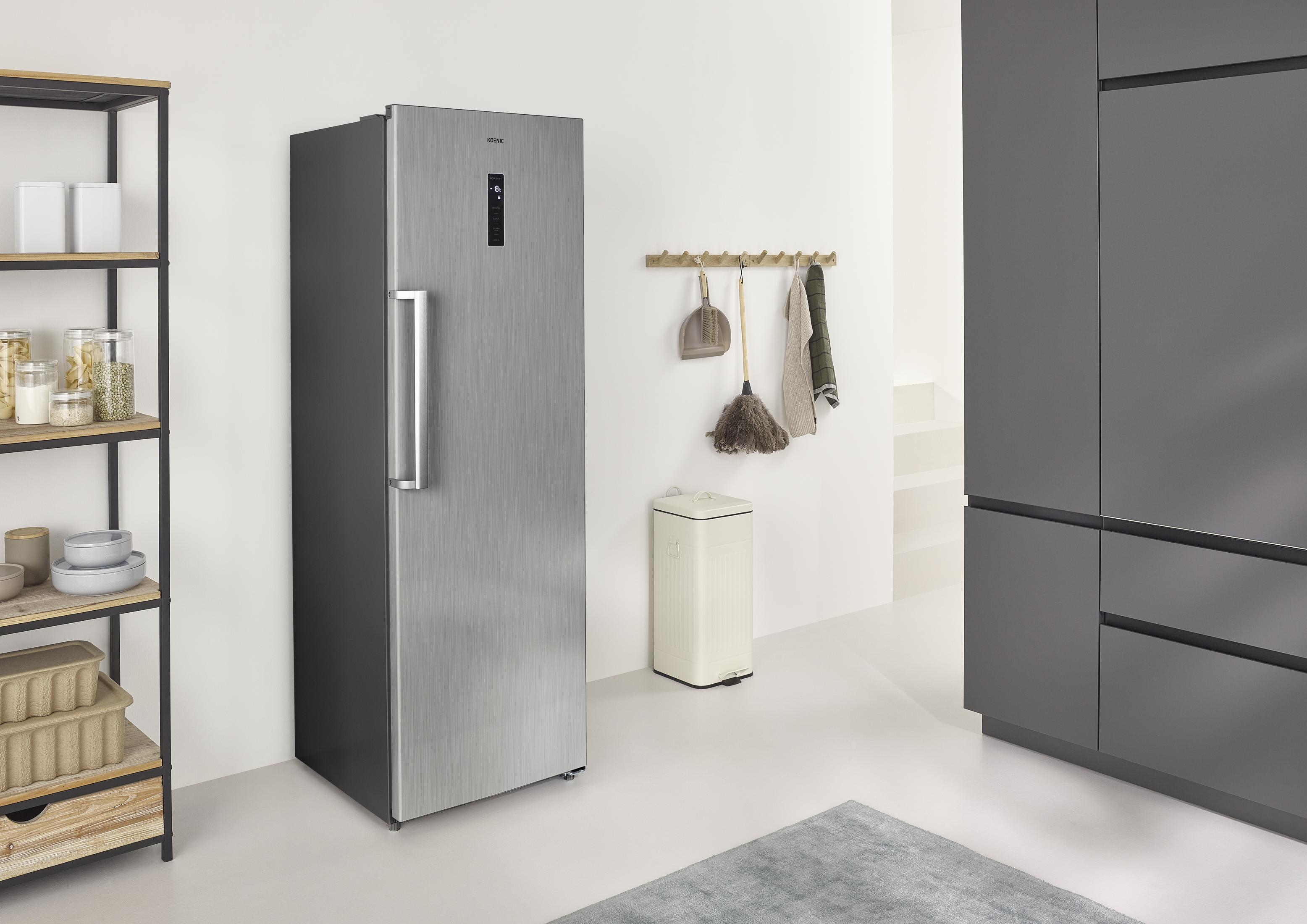 Ein silberner Kühlschrank steht neben einem Regal mit Vorräten und grauen Schränken.