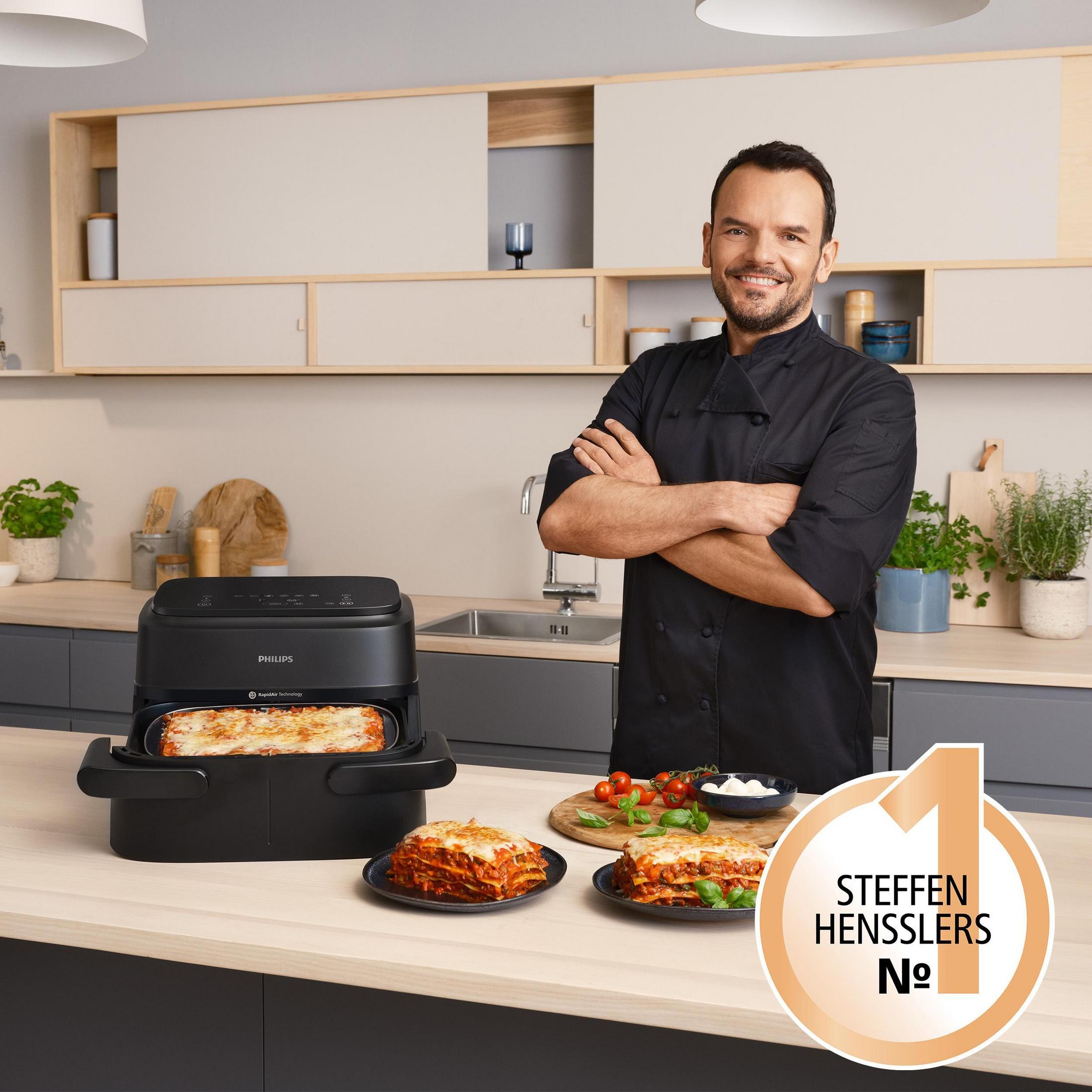 Un chef de negro junto a una freidora de aire Philips con lasaña.