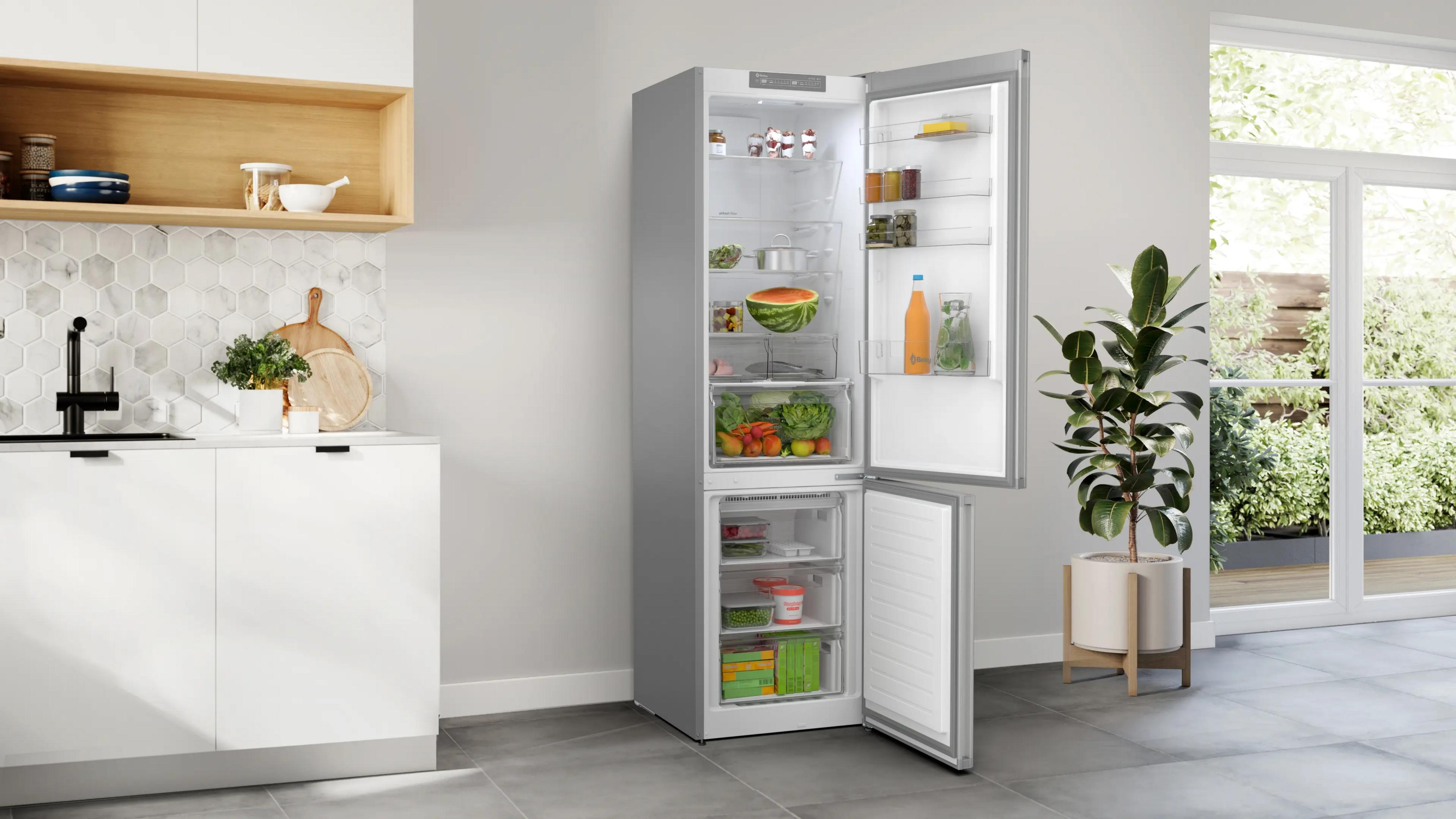 Refrigerador plateado abierto con comida y una planta al lado.