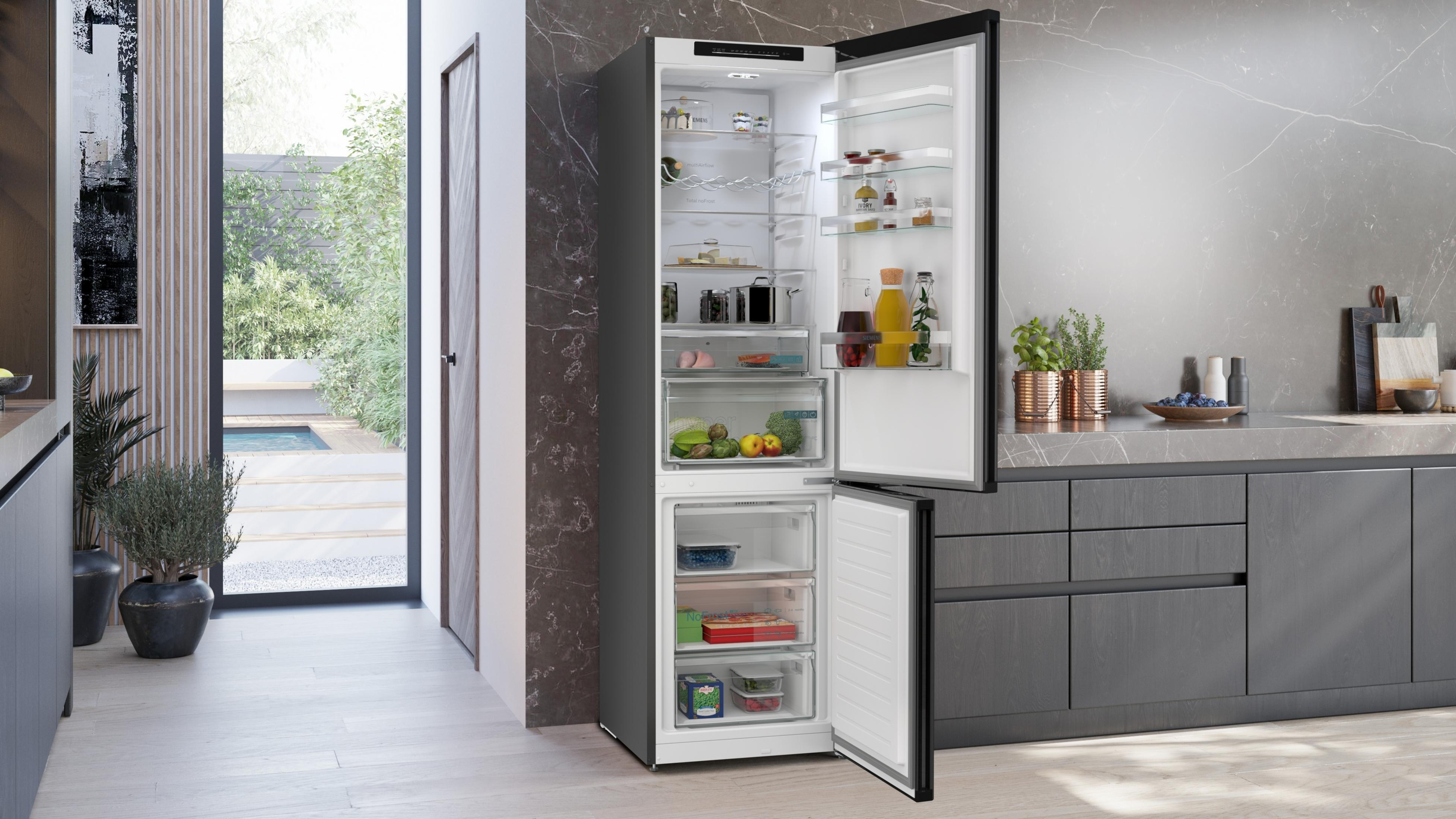 Offener Kühlschrank mit Lebensmitteln und Gefrierfach in einer modernen Küche mit Blick nach draußen.