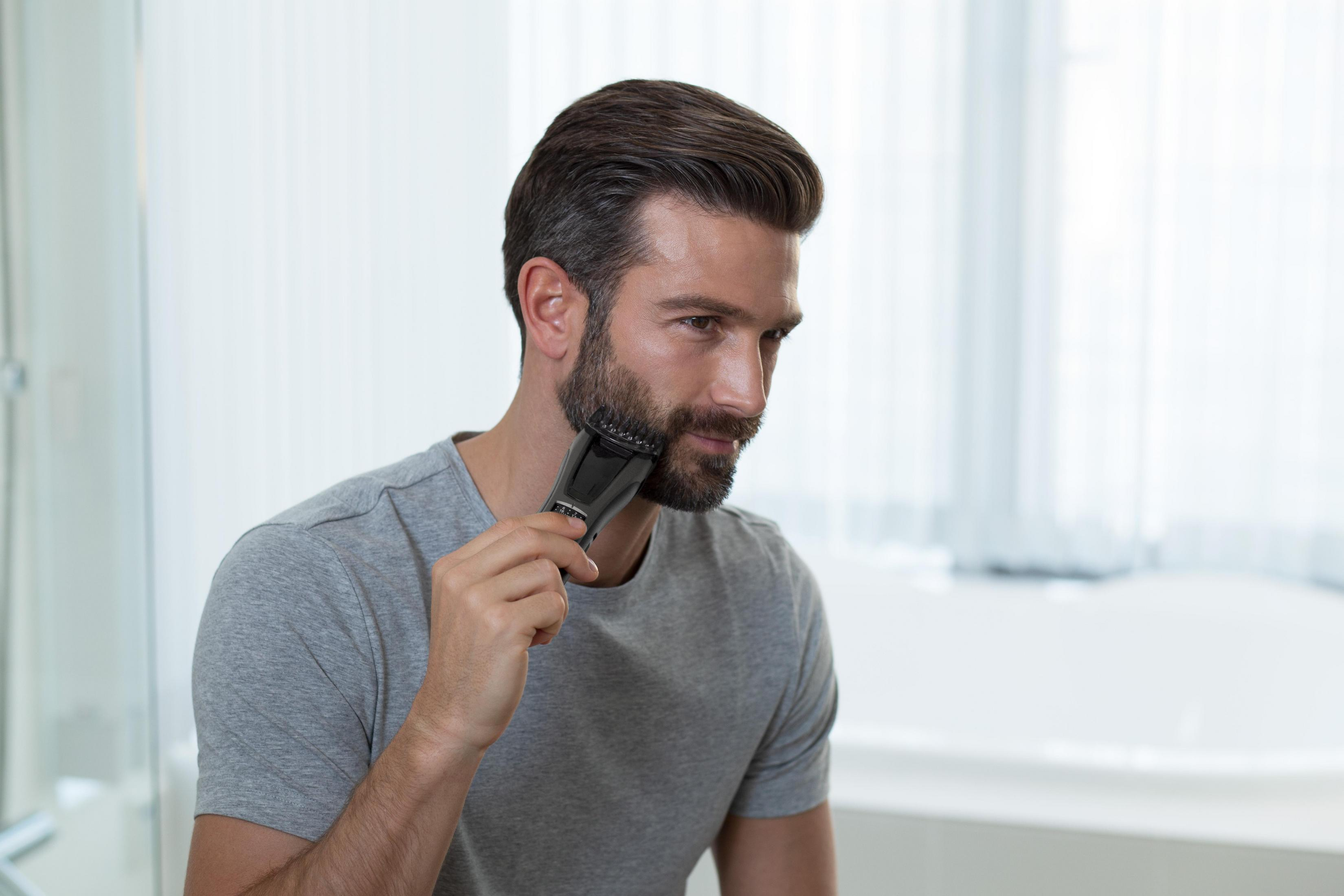Un uomo con la barba si taglia i peli del viso con un rifinitore nero.