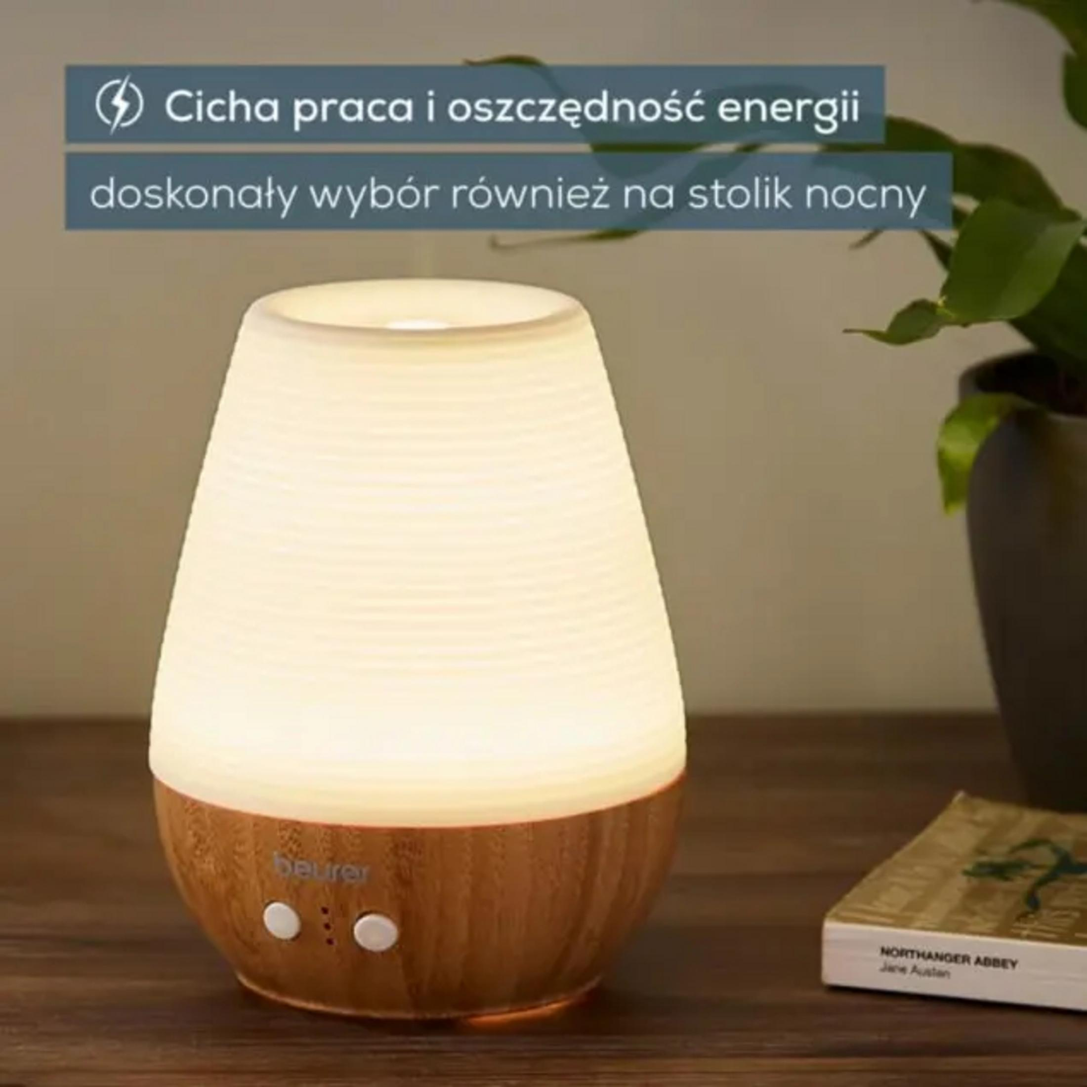 Ein beleuchteter Diffusor mit Holzbasis steht neben einem Buch und einer Pflanze.