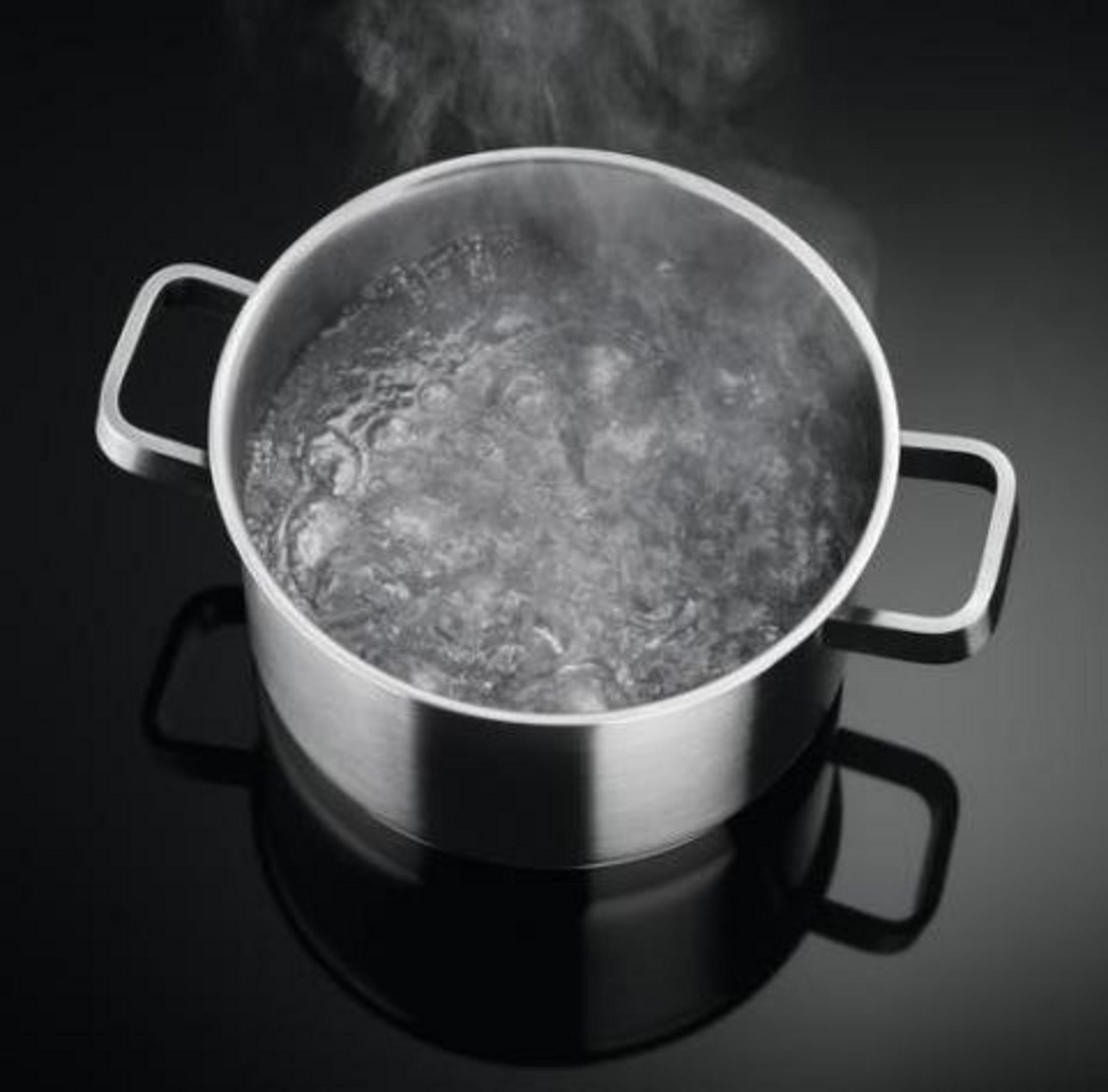 Una olla plateada con agua hirviendo y vapor sobre fondo negro.