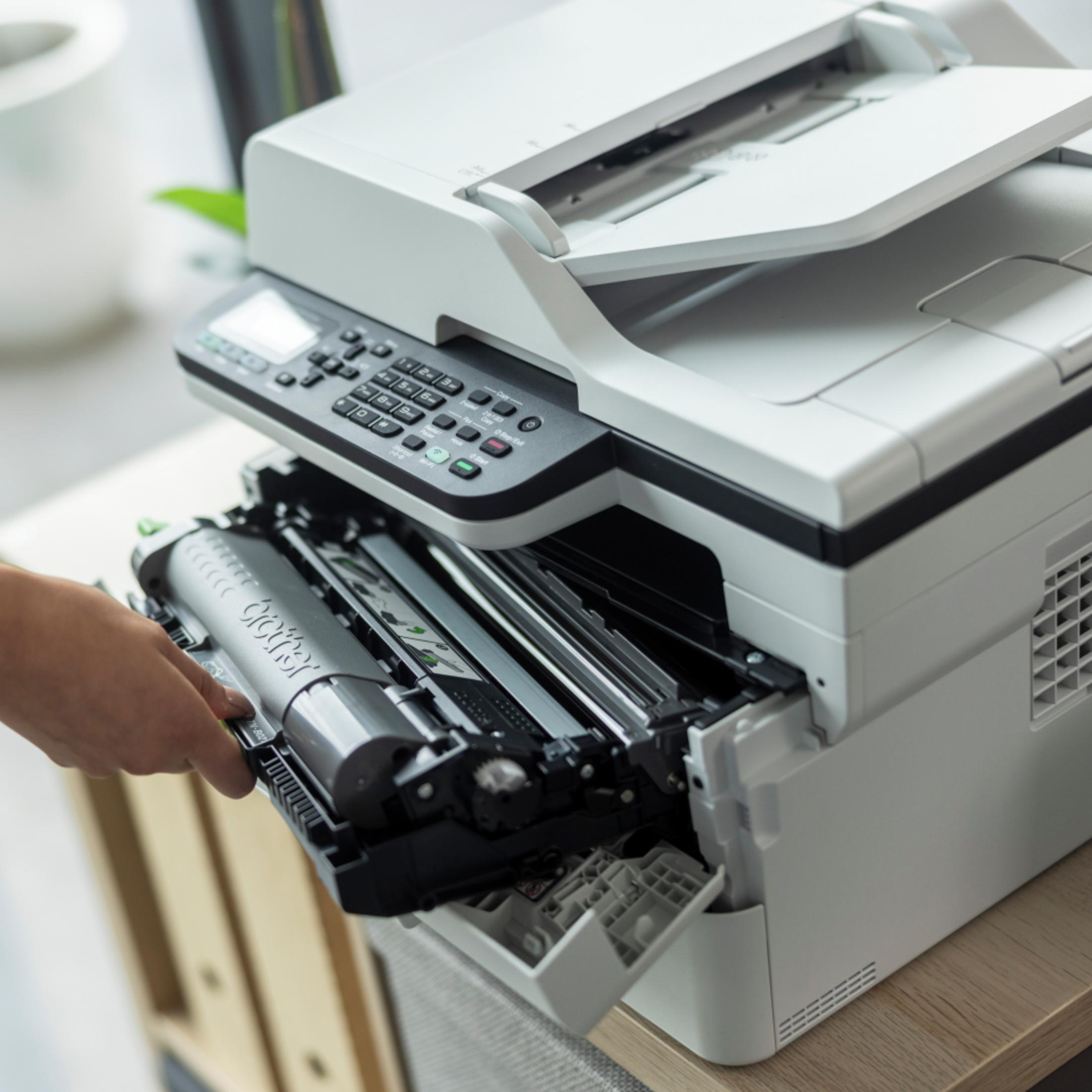 Eine Hand zieht eine Brother-Tonerpatrone aus einem weißen Multifunktionsdrucker.