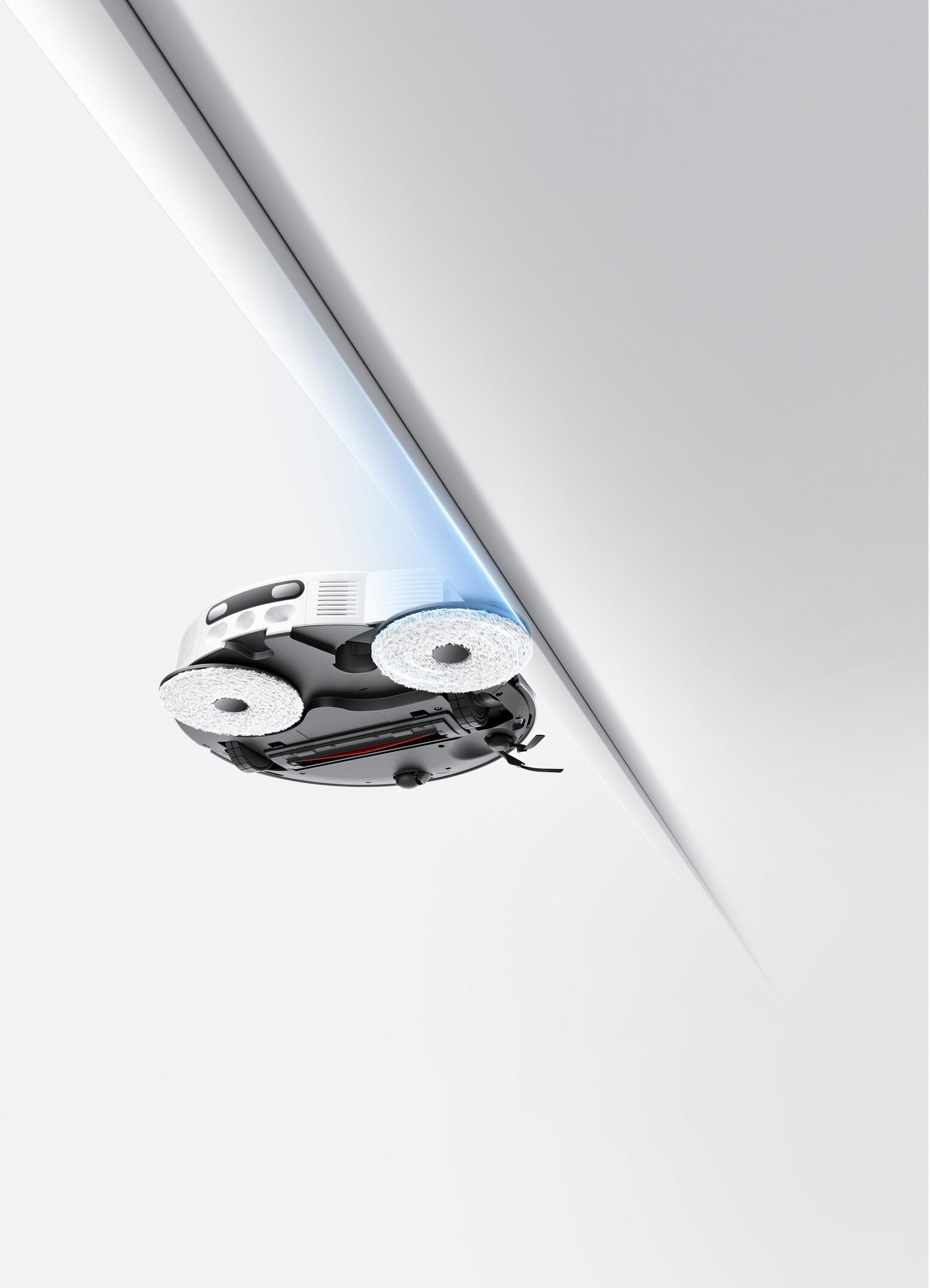 Dönen fırçalı beyaz robot süpürge beyaz bir köşeyi temizliyor.