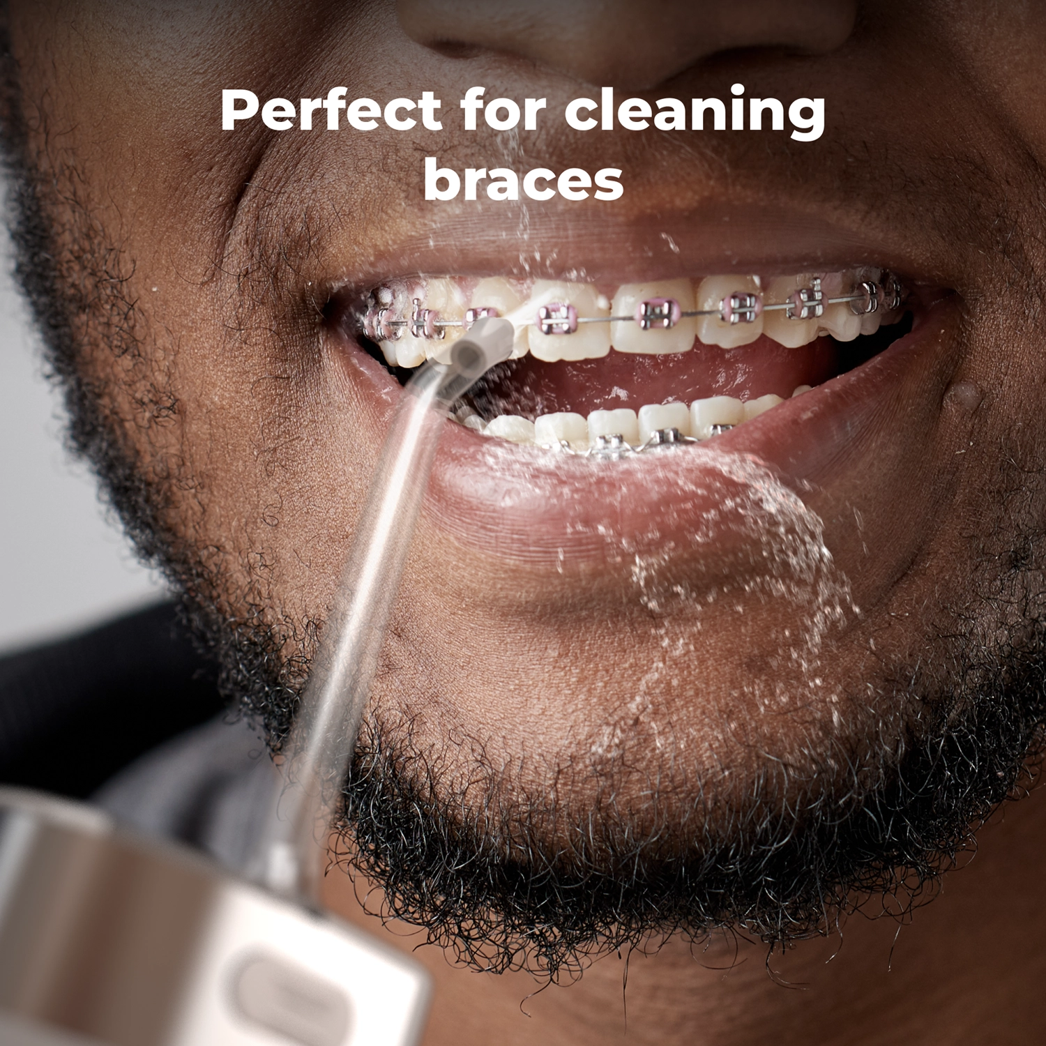 Close-up van een man met beugel die met water wordt besproeid door een waterflosser.