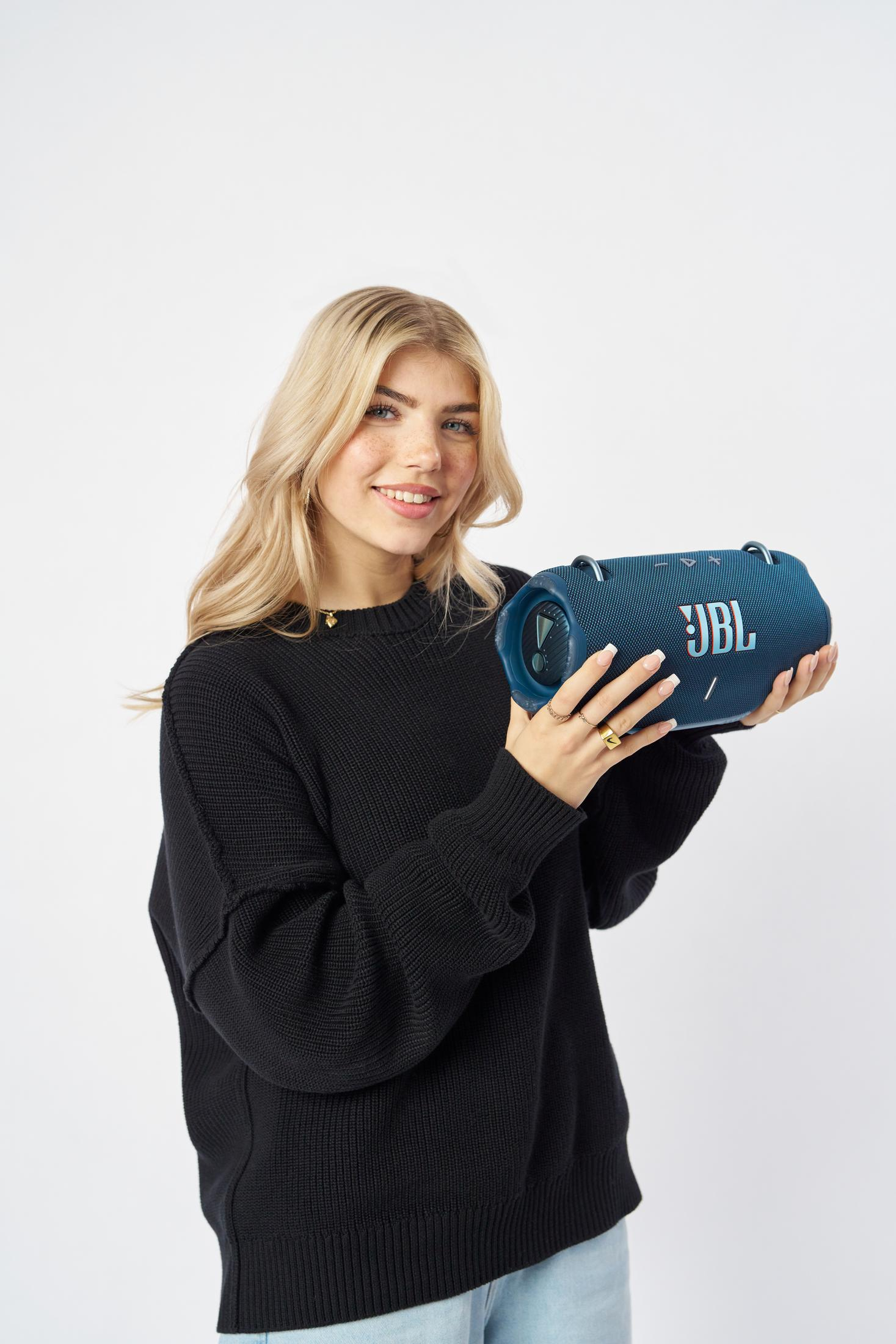 Una donna bionda tiene uno speaker JBL blu.