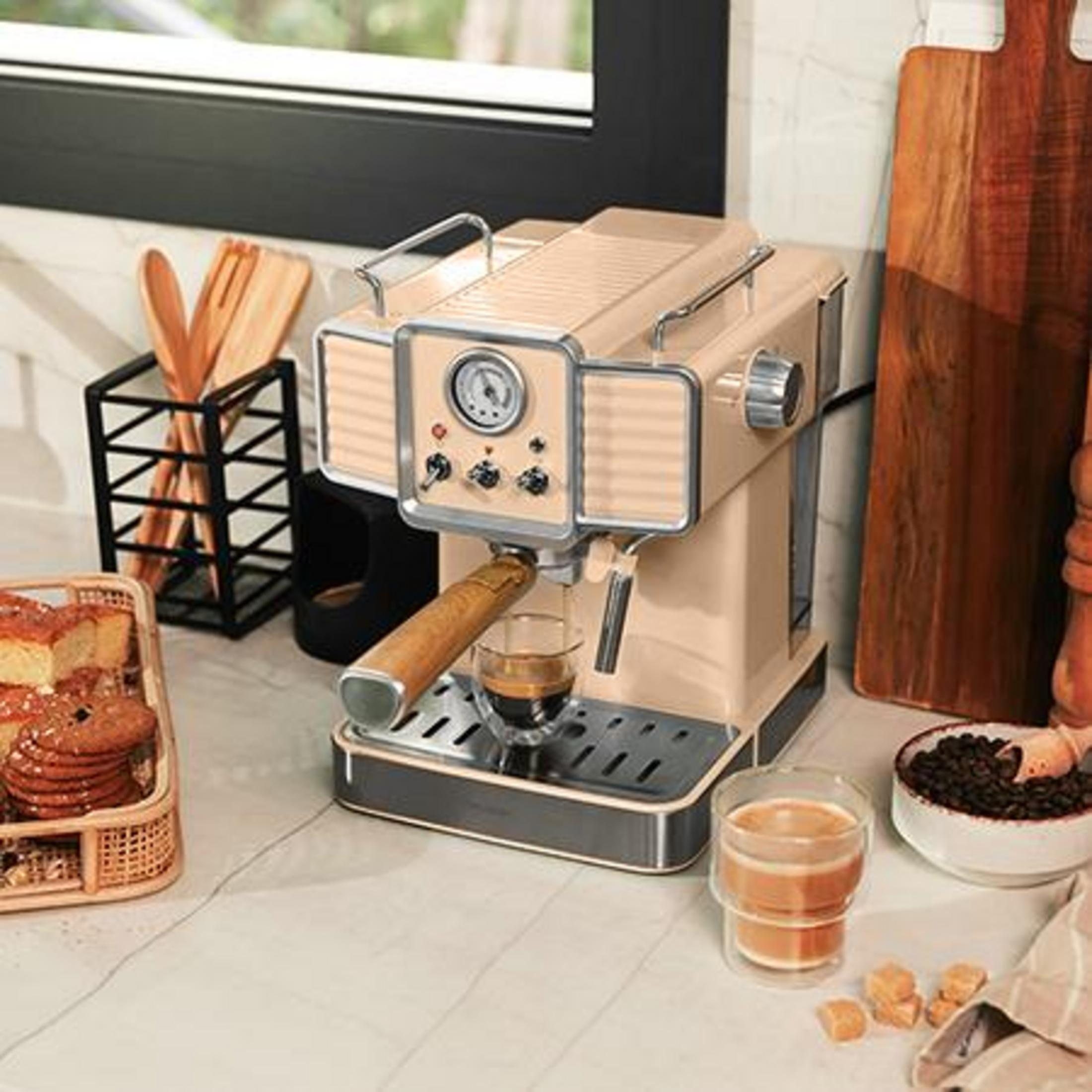 Una cafetera espresso color crema prepara café, con pasteles y granos de café cerca.