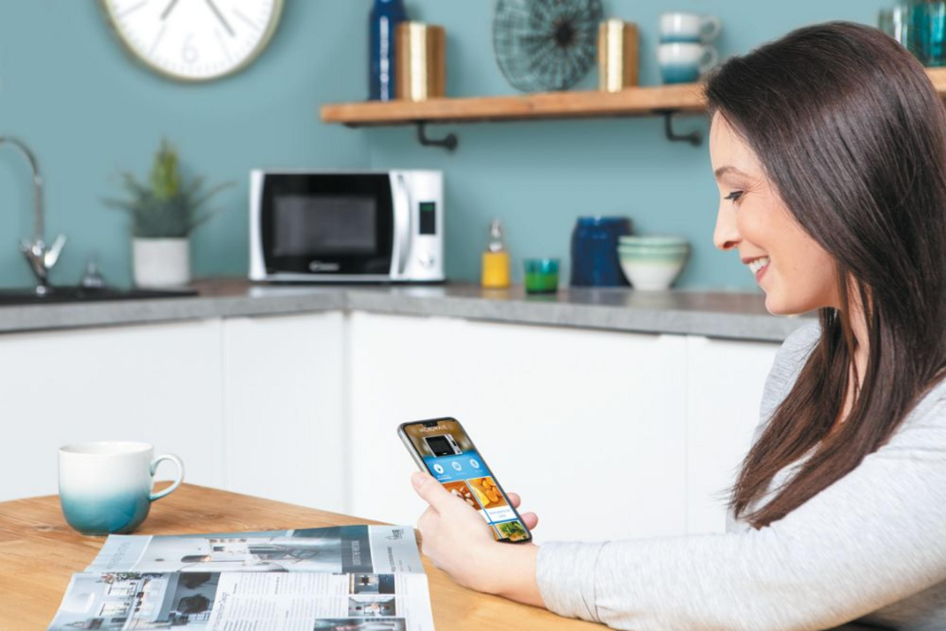 Donna guarda il telefono in cucina con microonde e tazza.