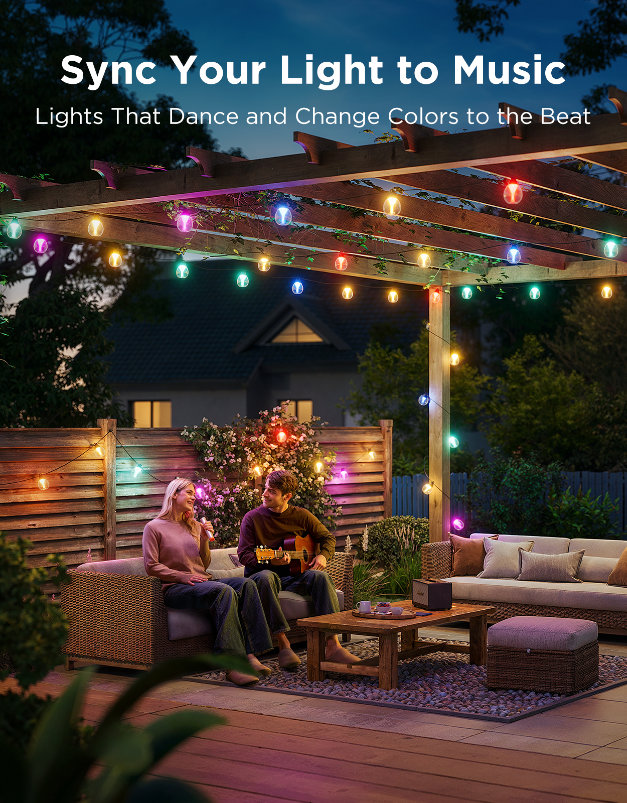 A couple on a patio at night, illuminated by colorful string lights. Man plays guitar.