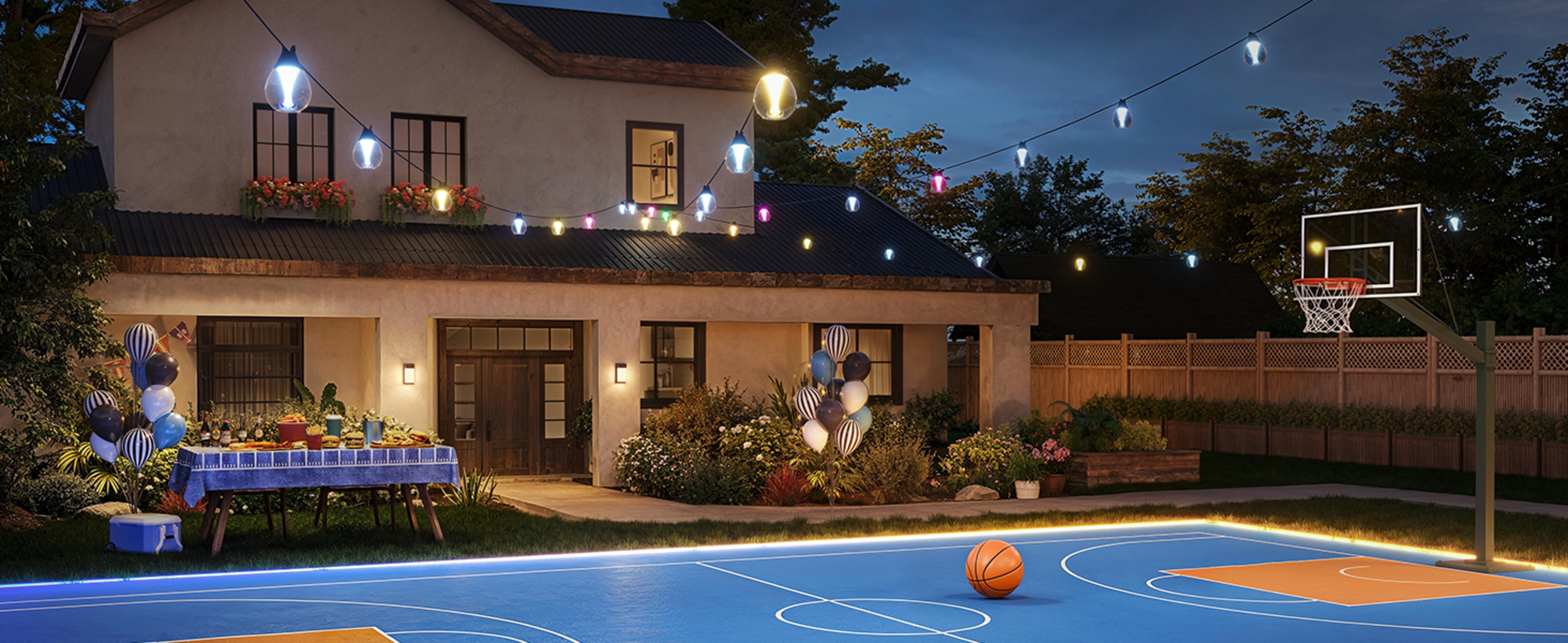 A backyard with a basketball hoop and party table under string lights at night.