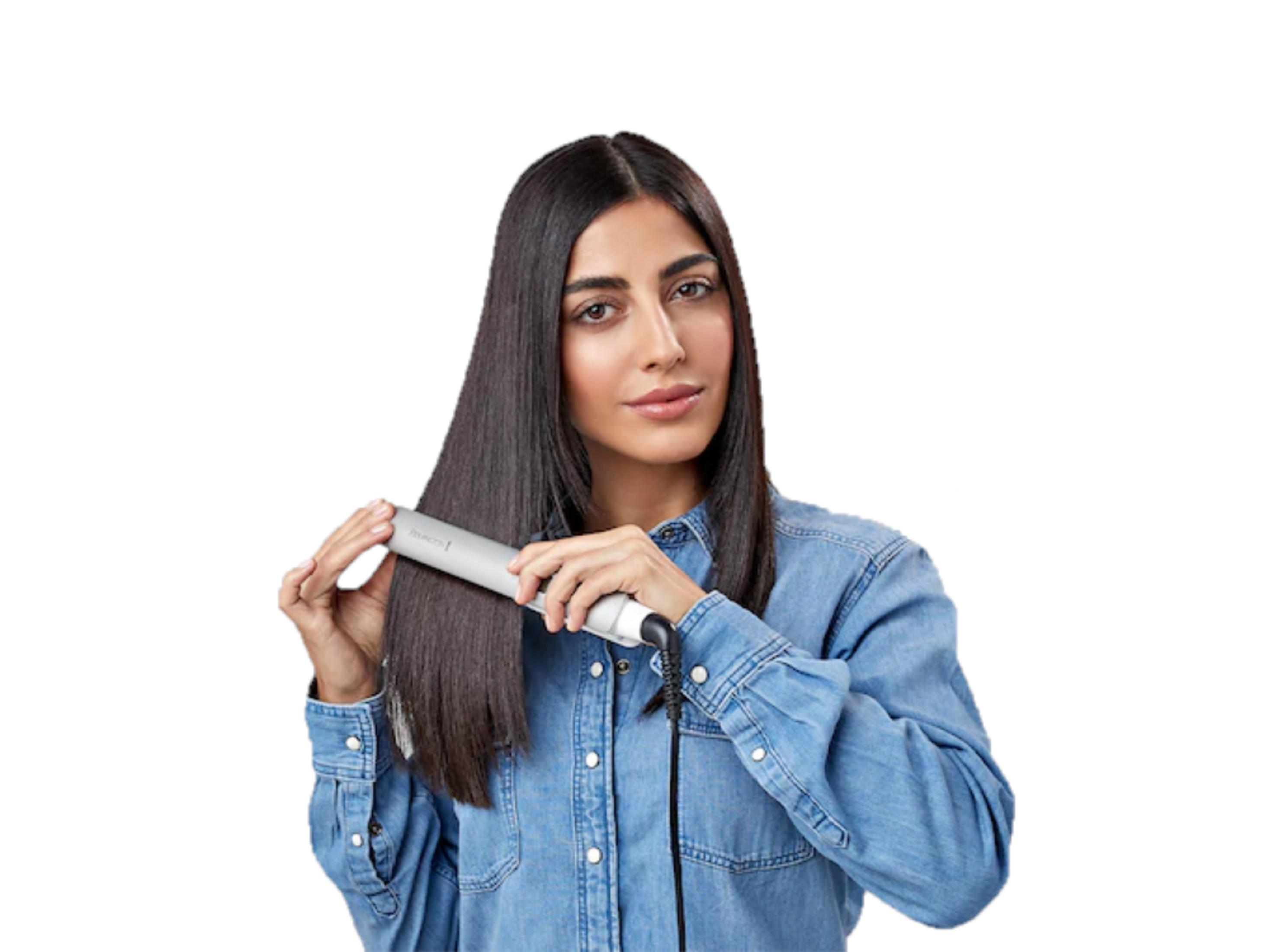 Una mujer de pelo largo y oscuro se alisa el pelo con una plancha gris.