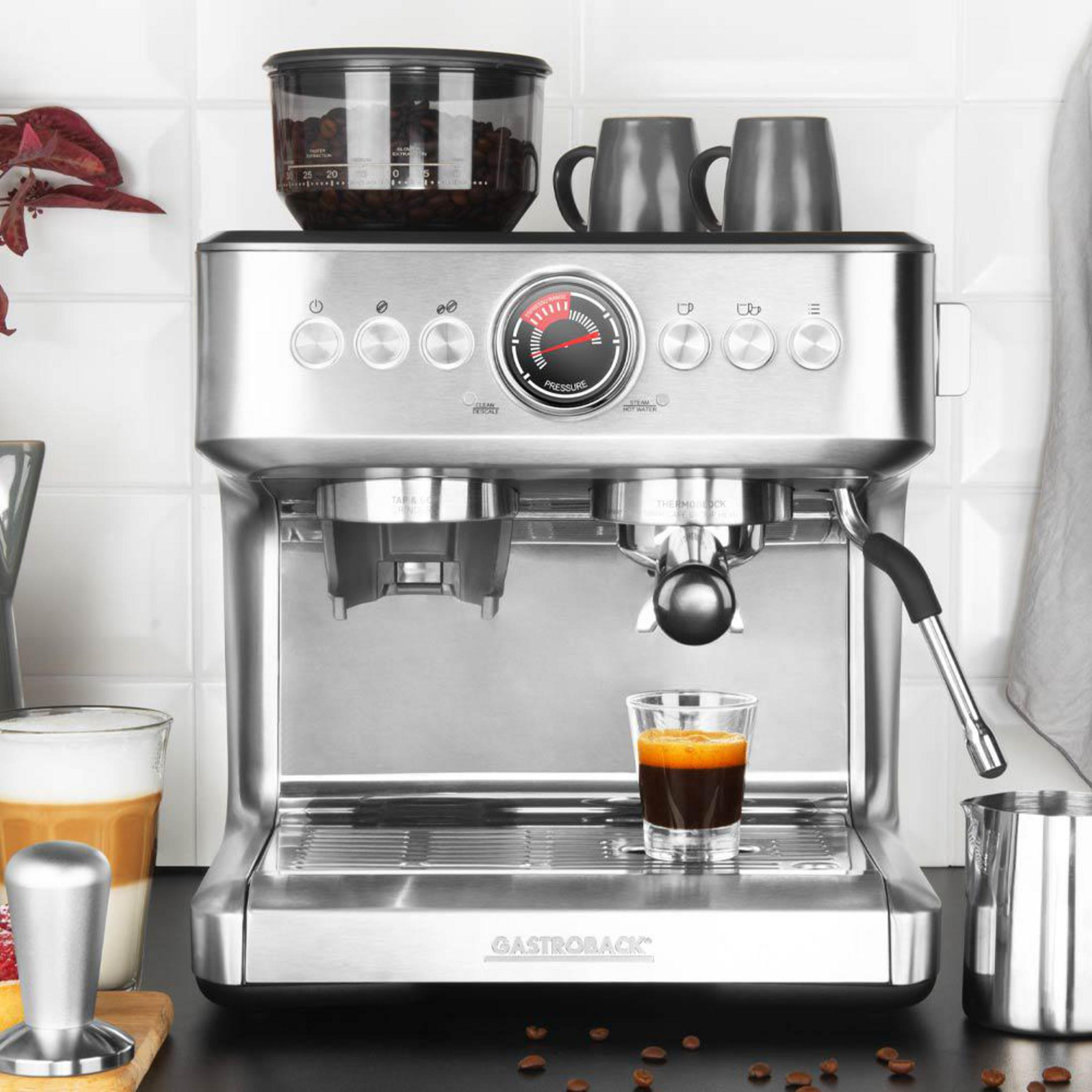 Una macchina per espresso argentata con bicchieri, tazze e chicchi di caffè.
